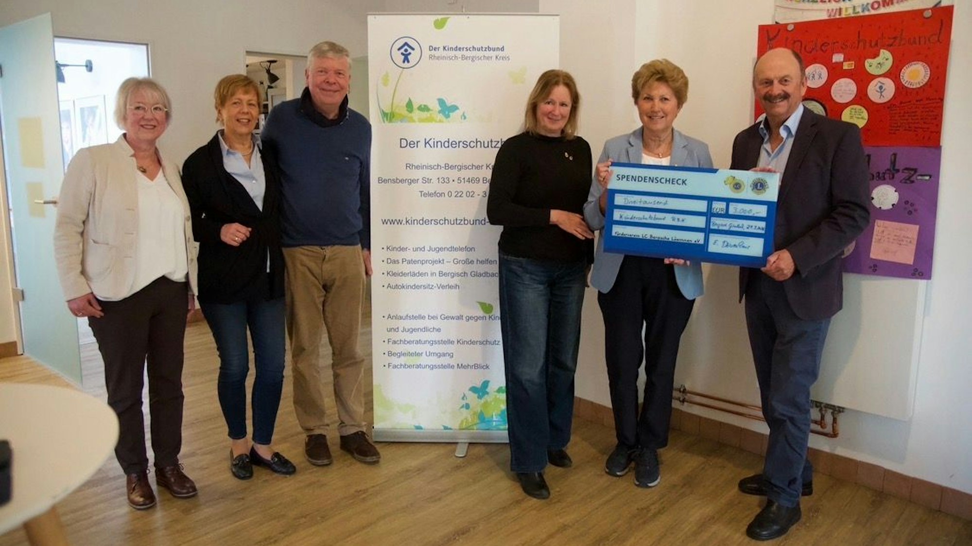Sechs Personen vor einem Plakat des Kinderschutzbundes, drei halten einen großen Spendenscheck.