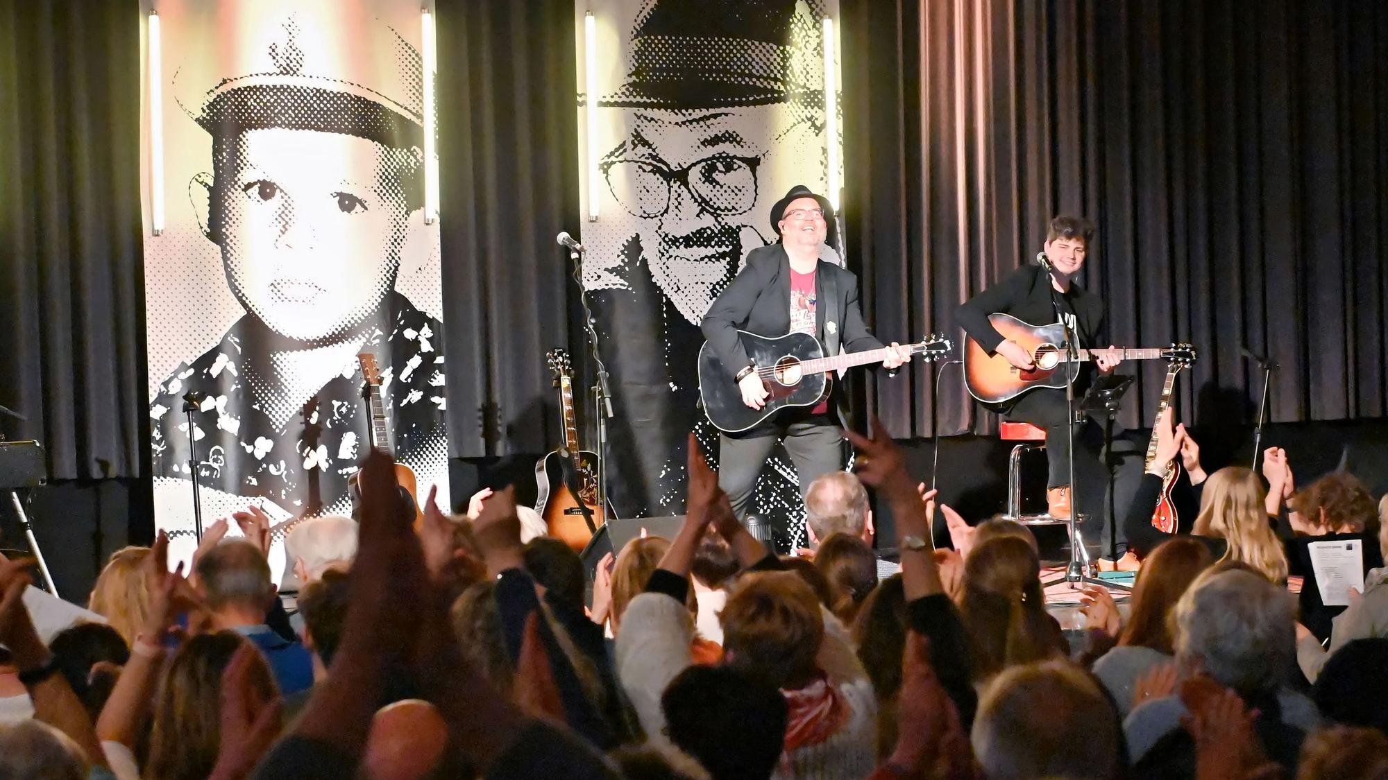 Auf der Bühne im Casino steht Björn Heuser mit seiner Band. An der Wand dahinter hängen große Banner mit Porträtfotos des Künstlers.