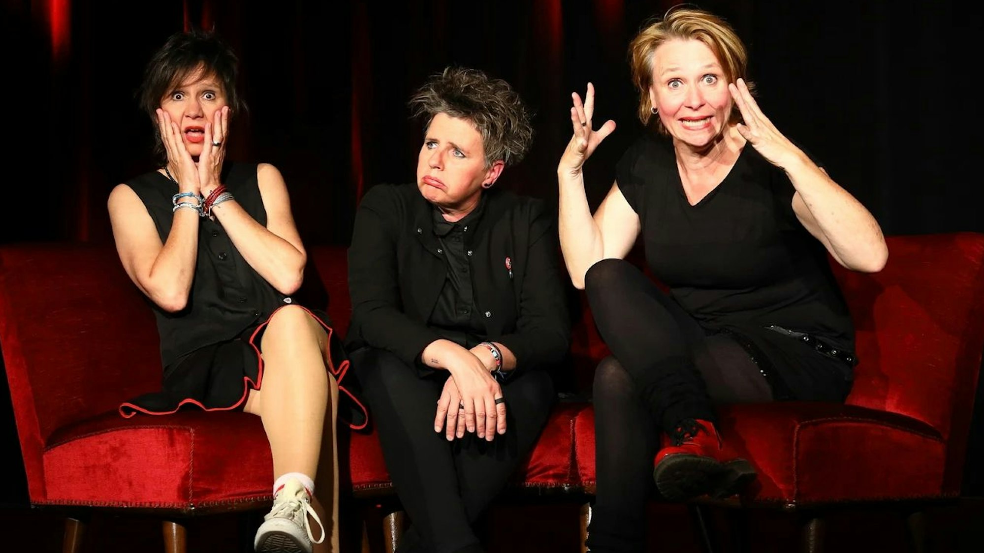 Drei Frauen, die Mitglieder des Kölner Trios „Abends mit Beleuchtung“, sitzen auf einem roten Sofa.