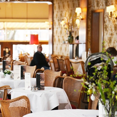 Der Gastraum ist zu sehen mit in Reihe stehenden kleinen runden Café-Tischen.