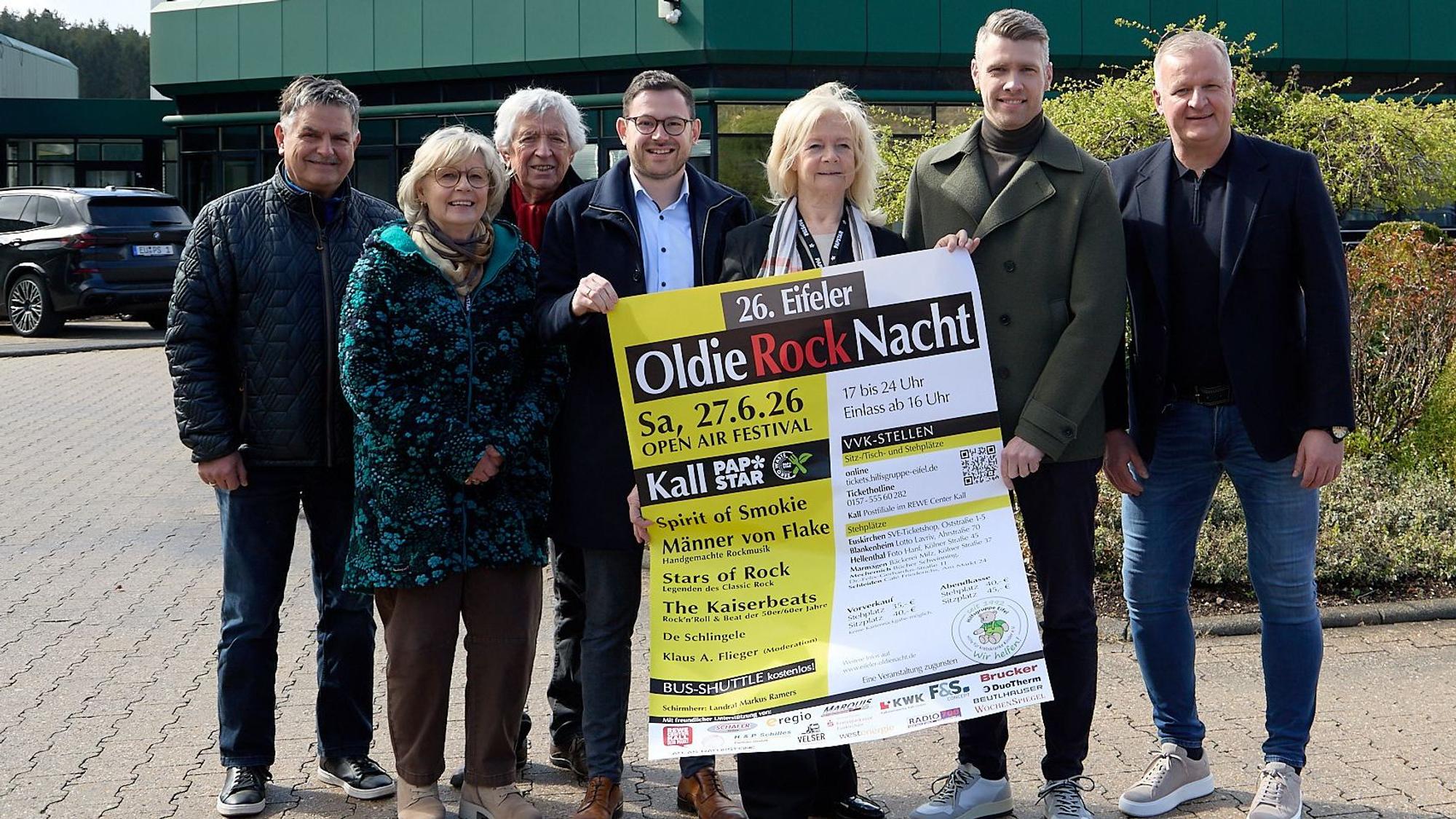 Fünf Männer und zwei Frauen stehen vor der Papstar-Zentrale in Kall und halten ein Plakat der Oldie-Nacht in die Kamera.