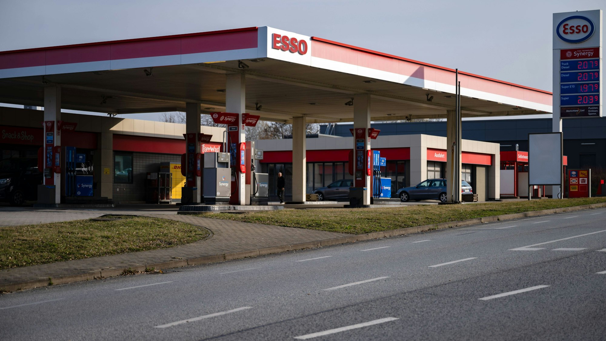 Tankstelle mit Preistafel, Fahrzeugen und Menschen
