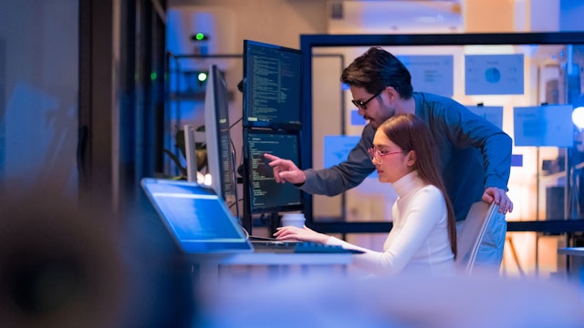 Asian programmers collaborating on software development at night, focused on writing code across multiple monitors in a tech office environment Programmers Collaborating on Software Development
