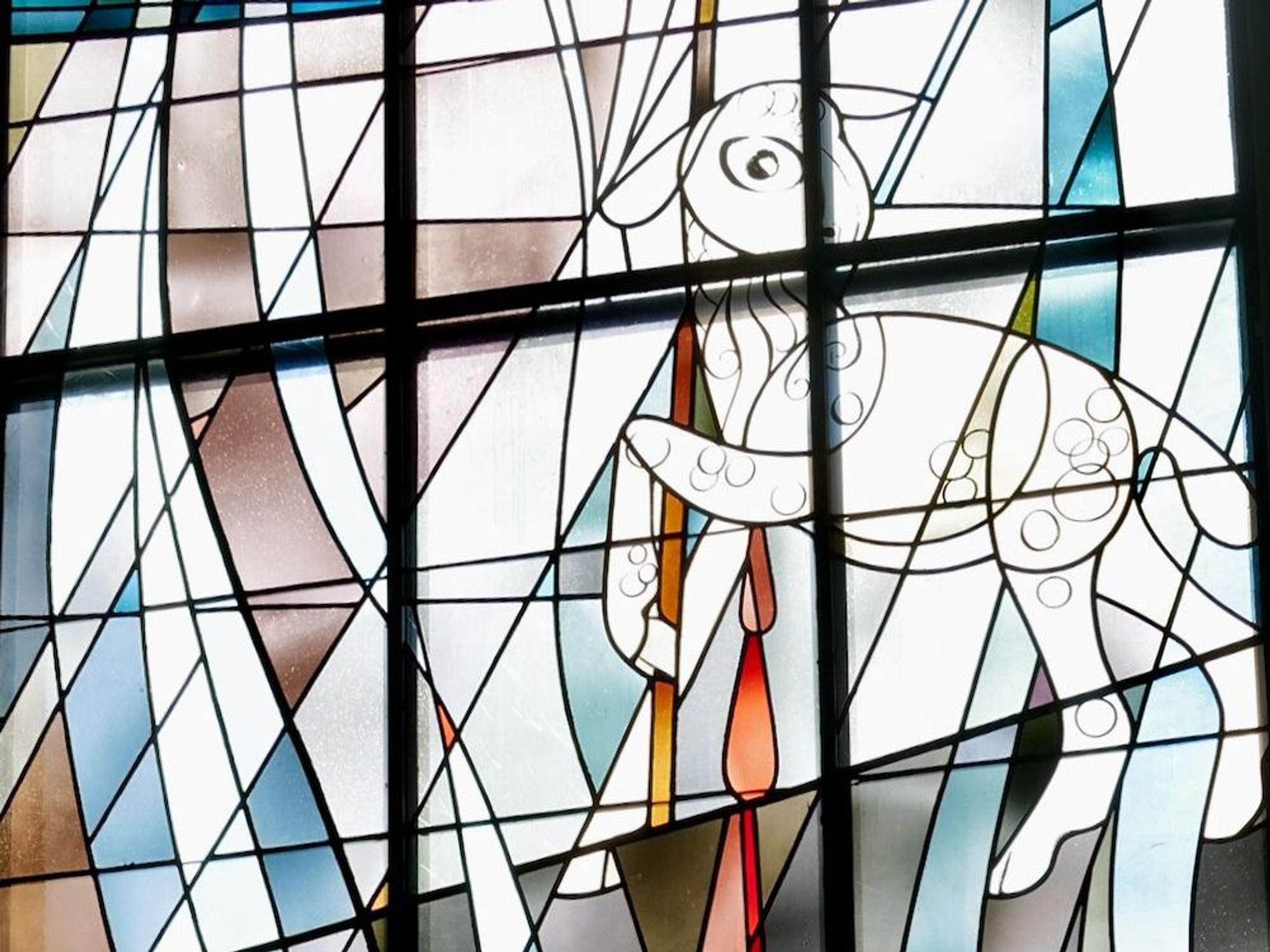 Das sechste Fenster steht für die Zeit der Kirche: Ein Lamm trägt die evangelische Kirchenfahne mit lila Kreuz auf weißem Grund. Blut tropft vom Lamm in einen Kelch.