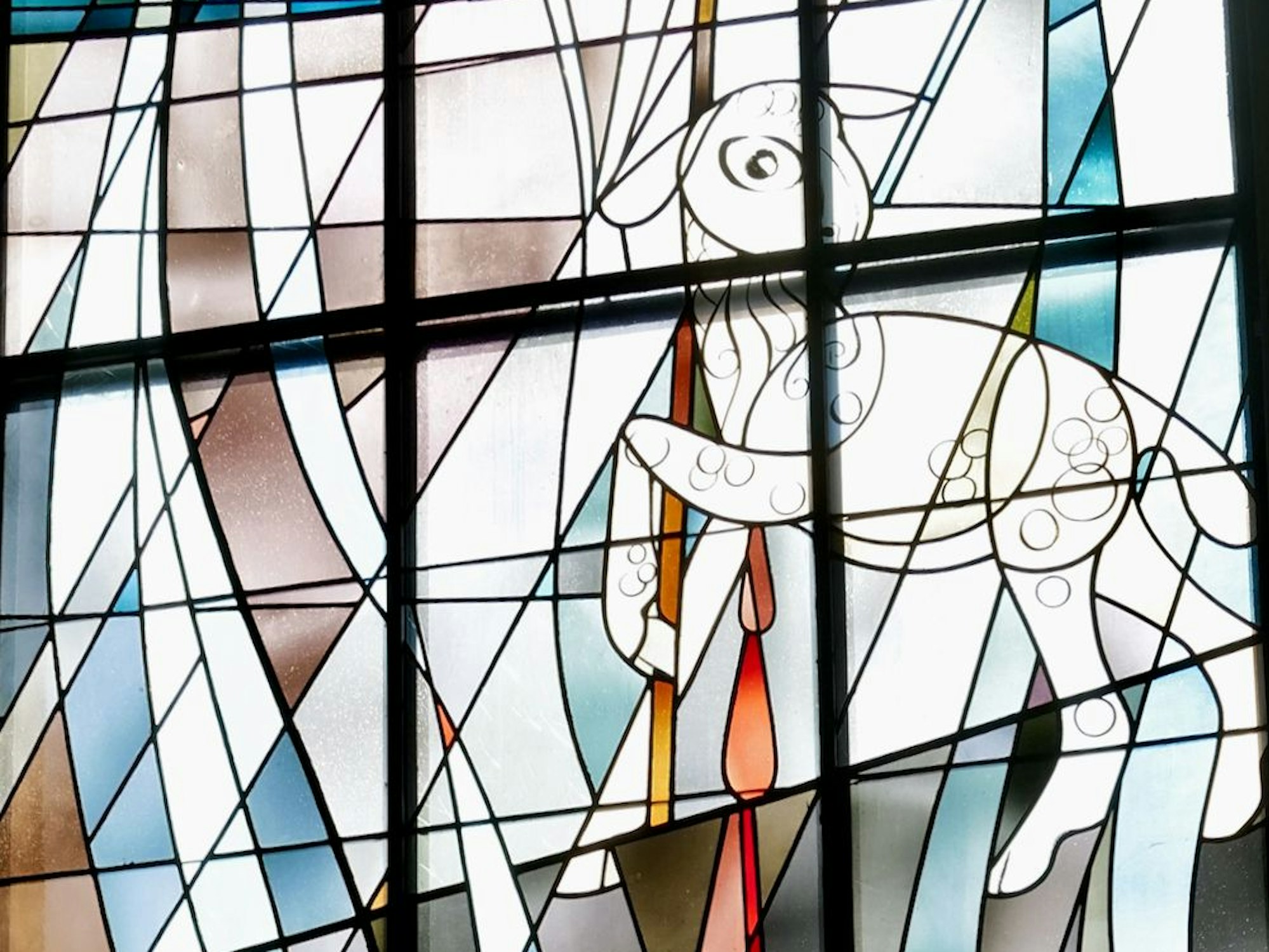Das sechste Fenster steht für die Zeit der Kirche: Ein Lamm trägt die evangelische Kirchenfahne mit lila Kreuz auf weißem Grund. Blut tropft vom Lamm in einen Kelch.