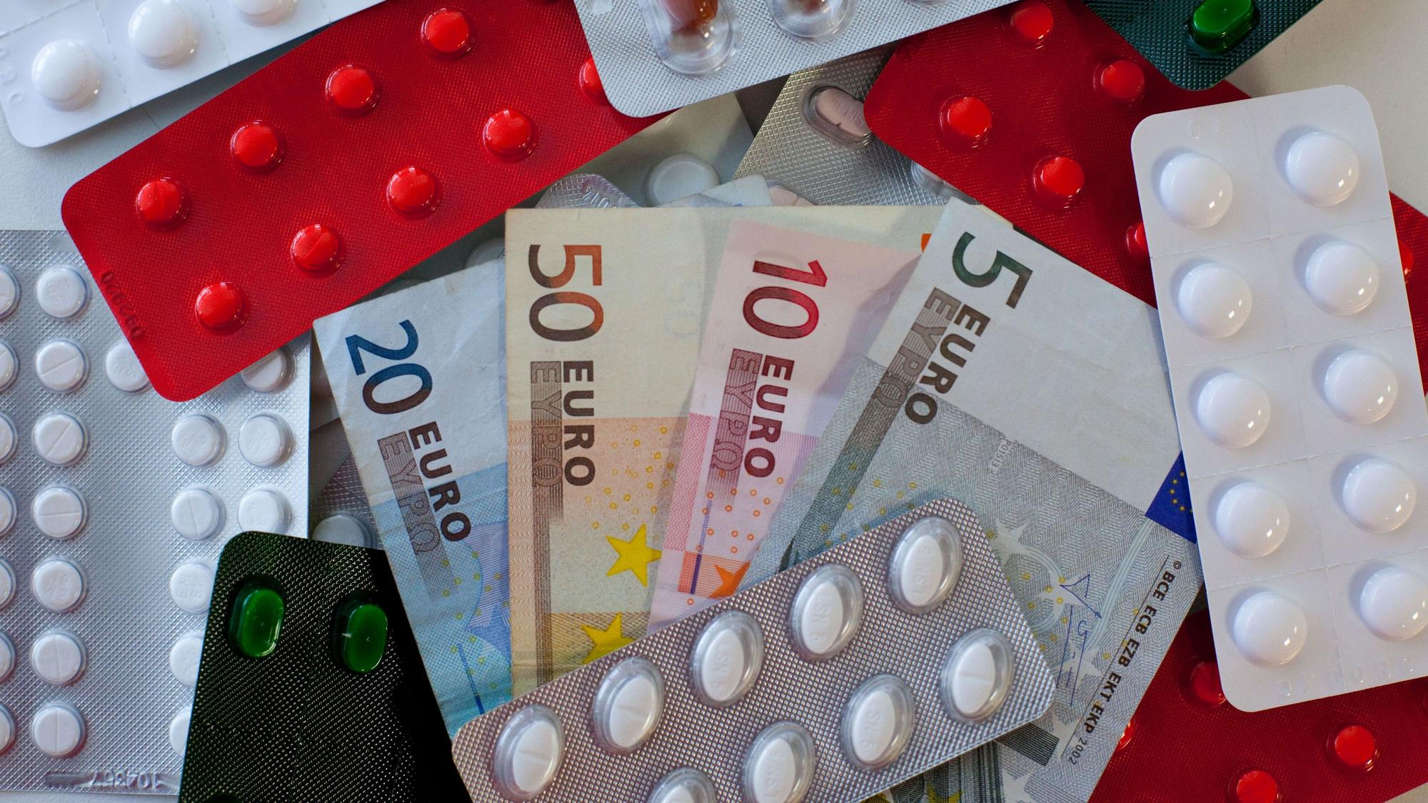 Tabletten und Euro-Scheine liegen auf einem Tisch einer Apotheke.