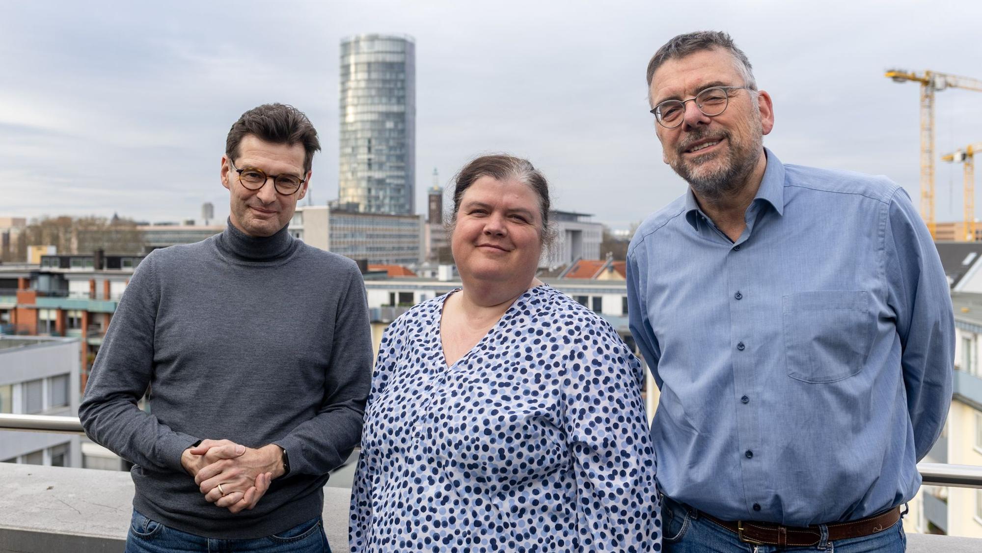 Zwei Männer und eine Frau in der Mitte schauen in die Kamera.