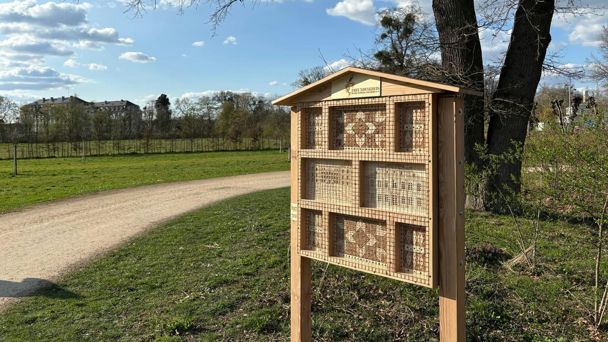 Ein Wildbienenhotel steht auf einer Wiese an einem Weg.