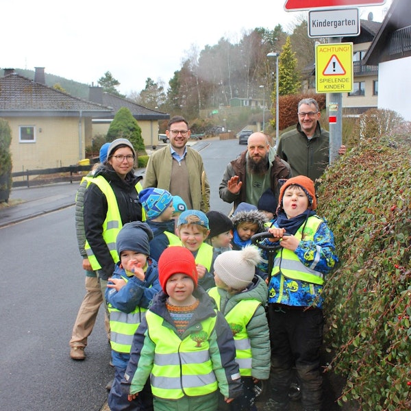 Das Bild zeigt drei Männer und eine Erzieherin mit den Kindern, die Warnwesten tragen.