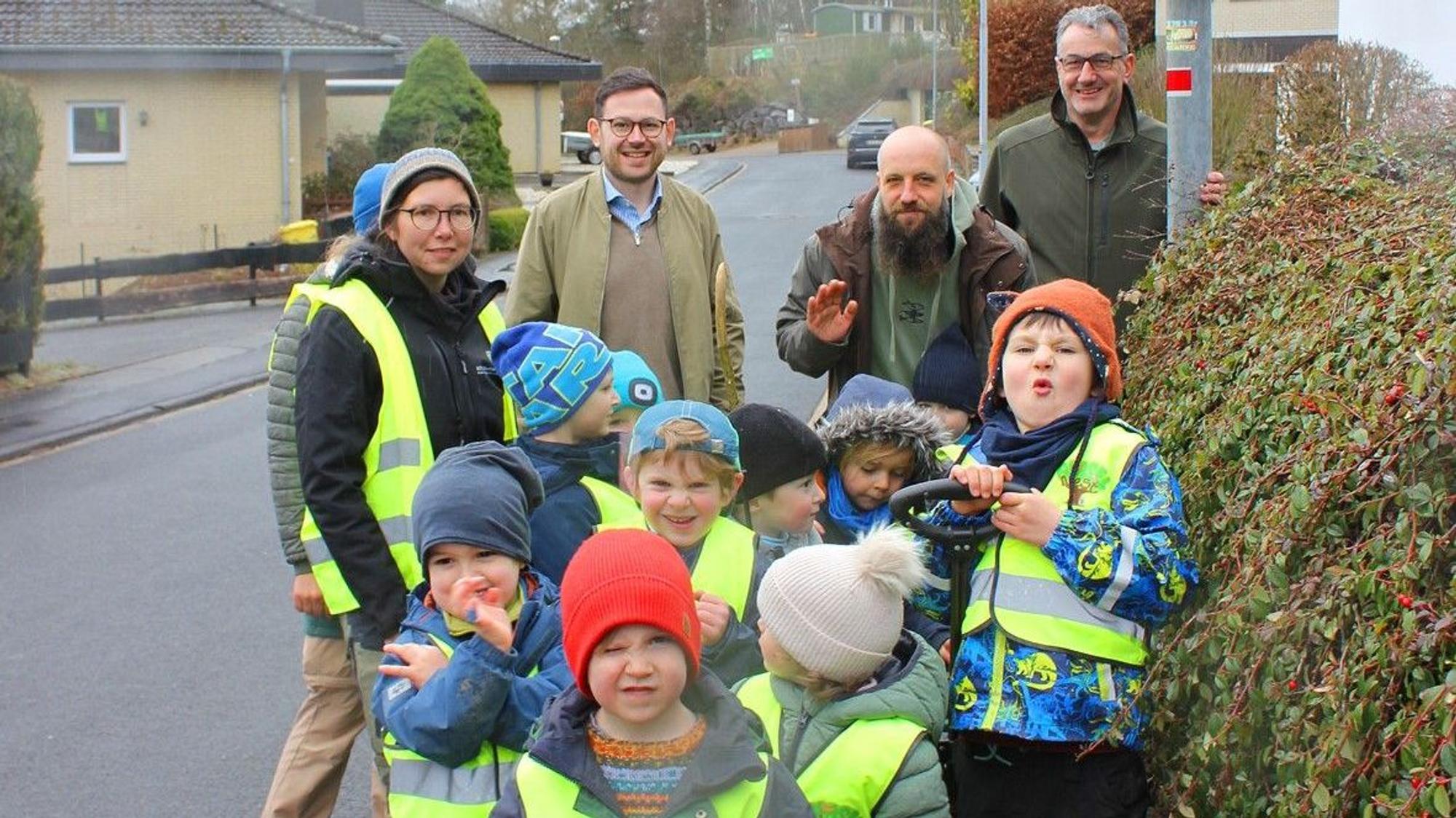Das Bild zeigt drei Männer und eine Erzieherin mit den Kindern, die Warnwesten tragen.