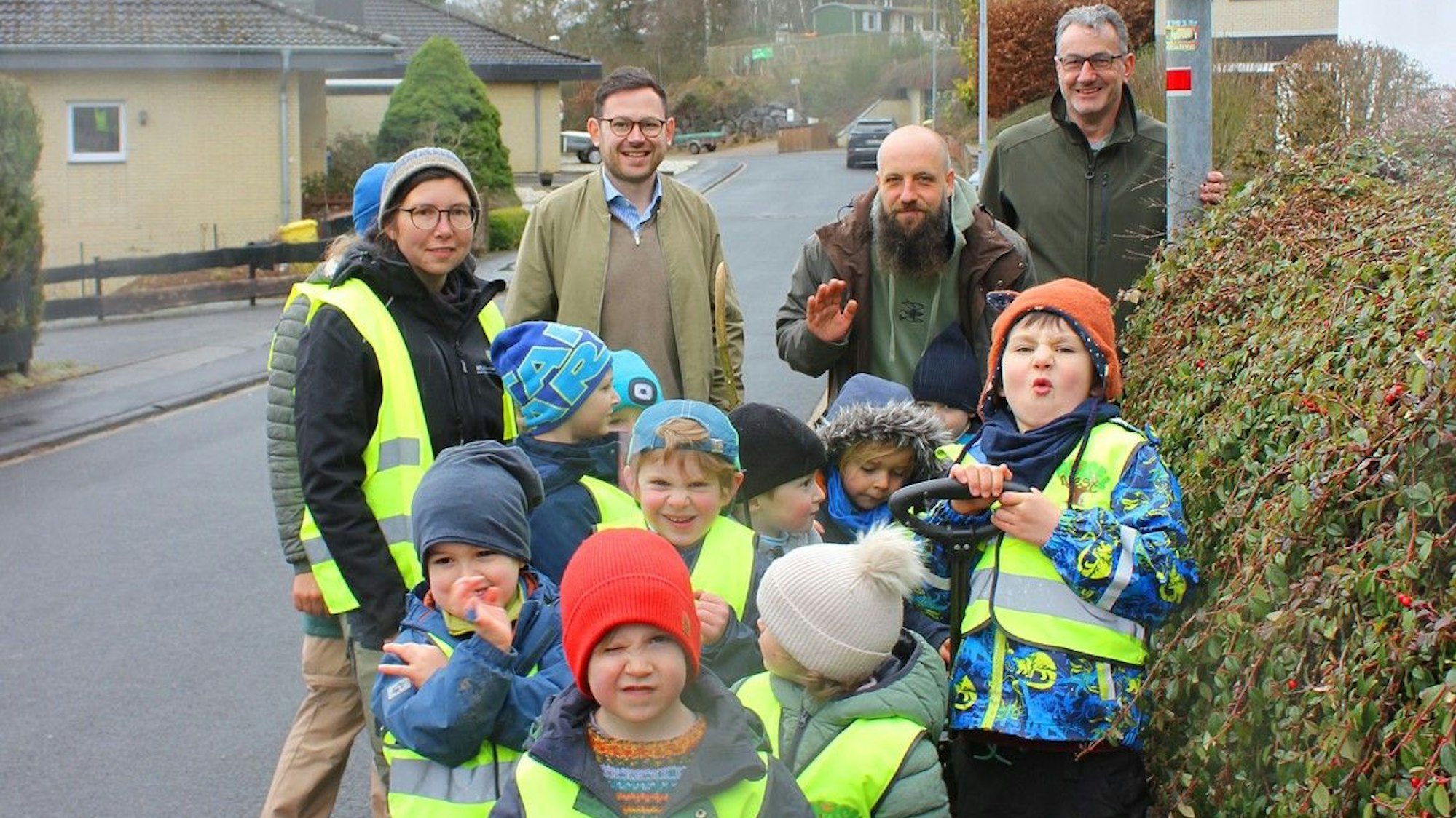 Das Bild zeigt drei Männer und eine Erzieherin mit den Kindern, die Warnwesten tragen.