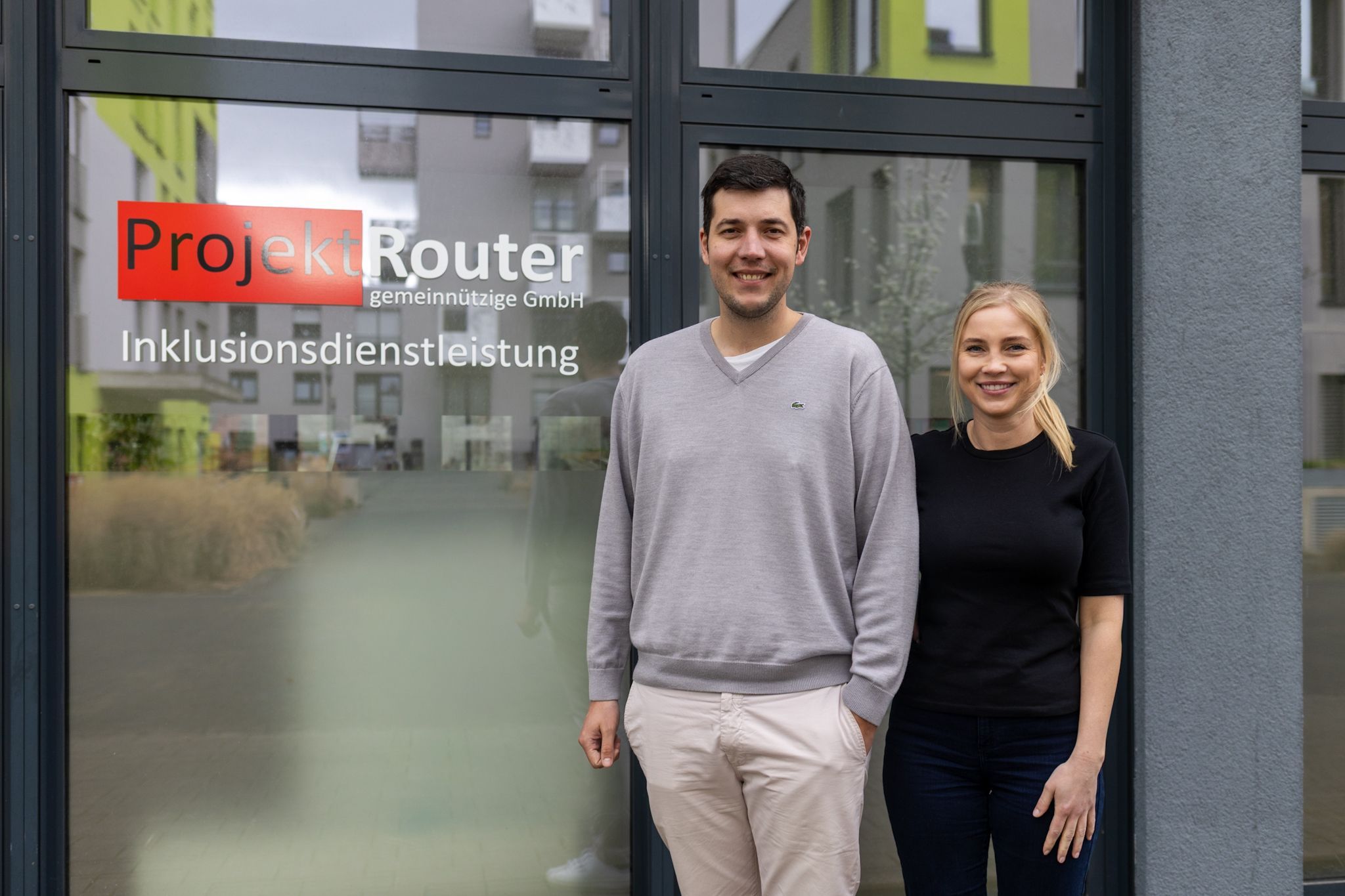 Ein Mann und eine Frau stehen vor einem Fenster mit der Aufschrift „Projekt Router“.