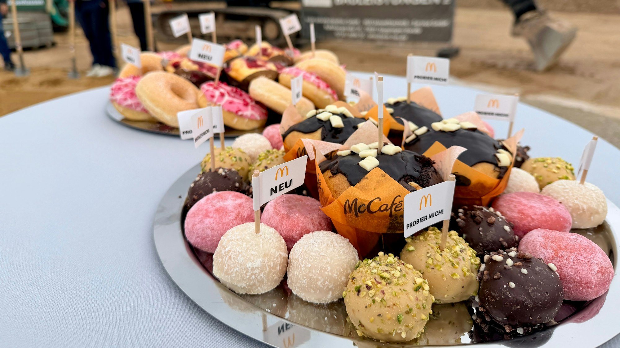 Muffins, Donuts und andere Leckereien von McDonald's, in denen kleine Fähnchen stecken, liegen auf einem Teller.