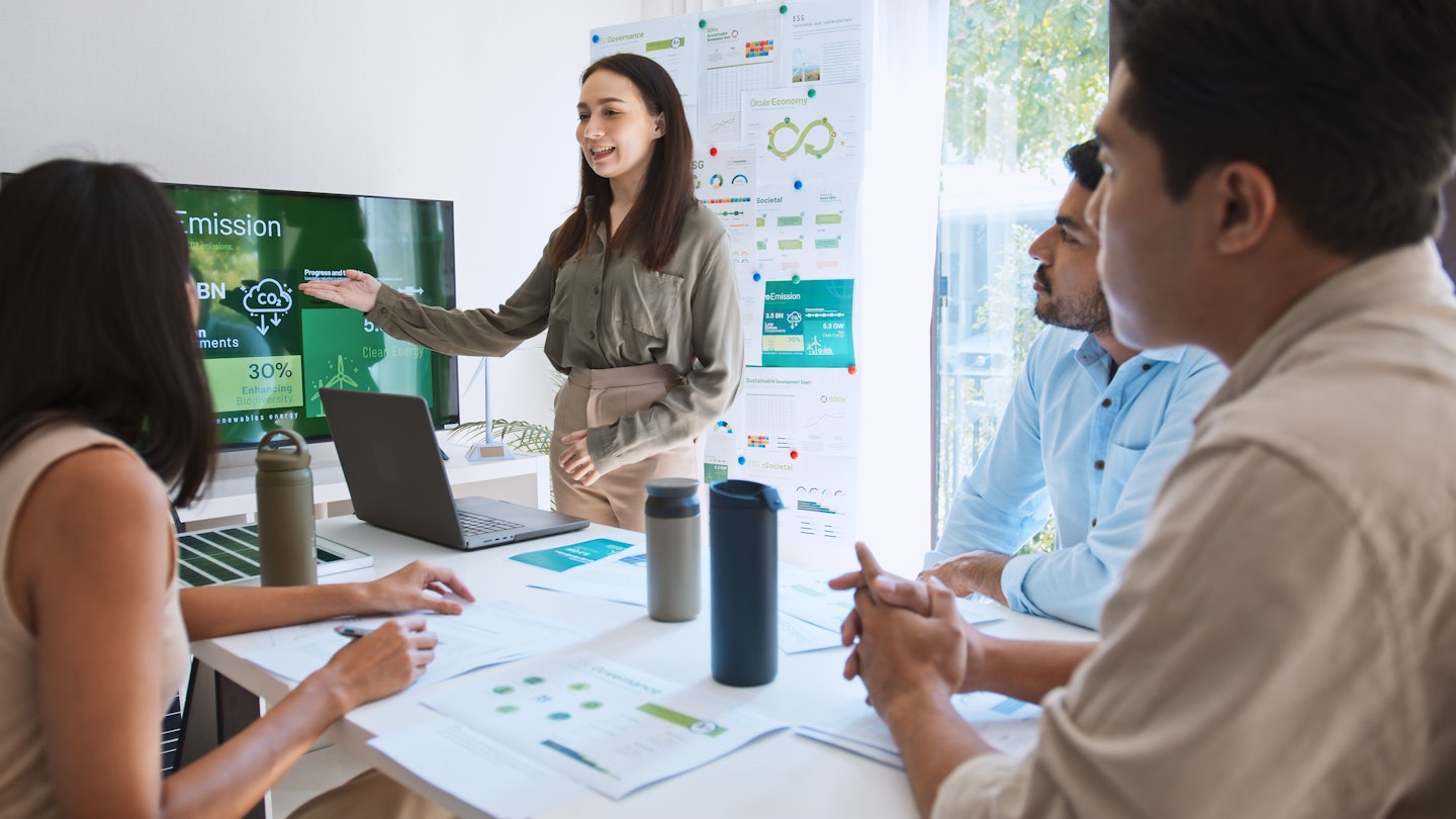 Eine Frau präsentiert ihrem Team in einem Meetingraum eine Nachhaltigkeitsstrategie.