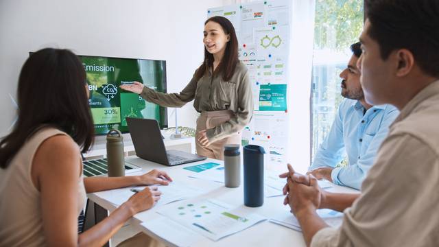 Eine Frau präsentiert ihrem Team in einem Meetingraum eine Nachhaltigkeitsstrategie.