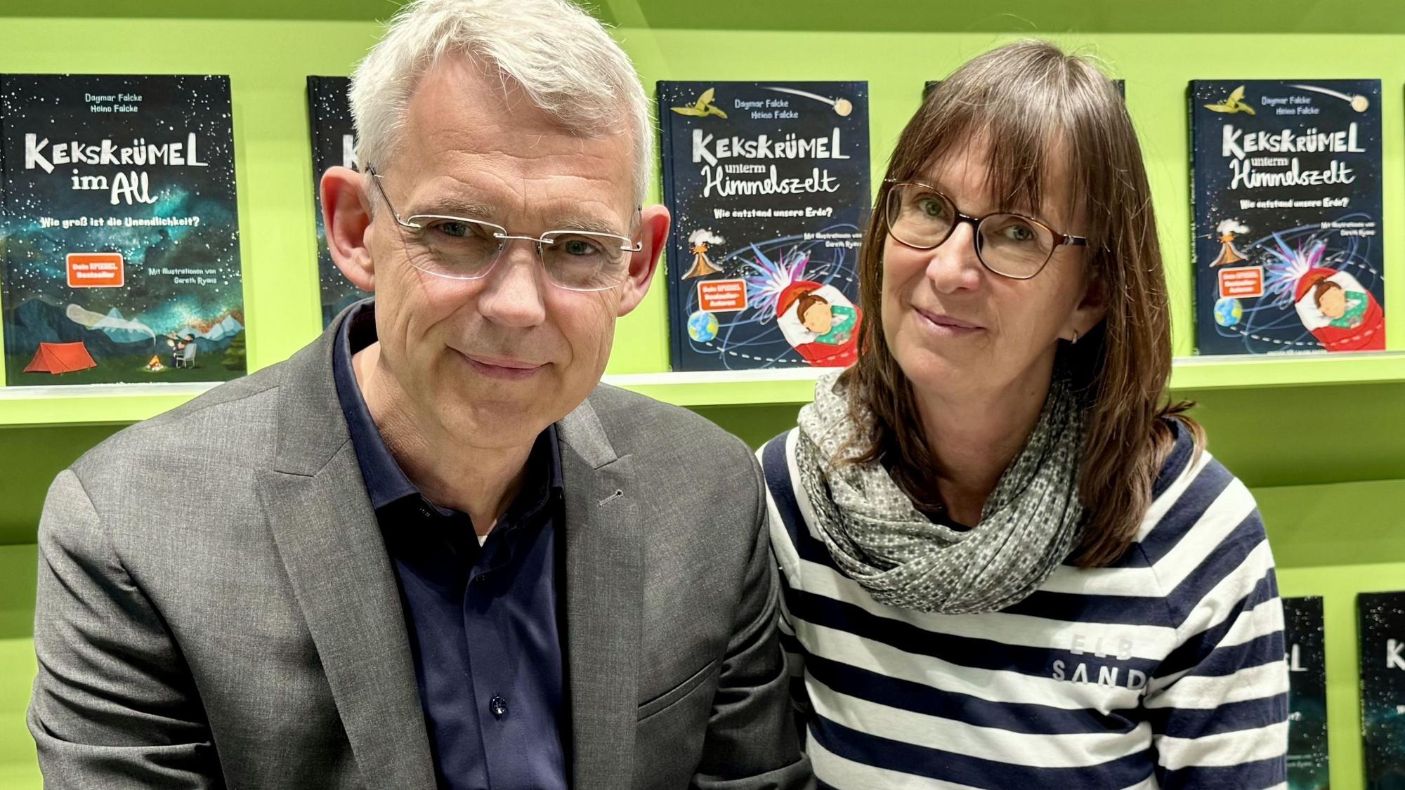 Eine Frau und ein Mann lächeln in die Kamera. Im Hintergrund sind Bücher in einem Regal zu sehen.