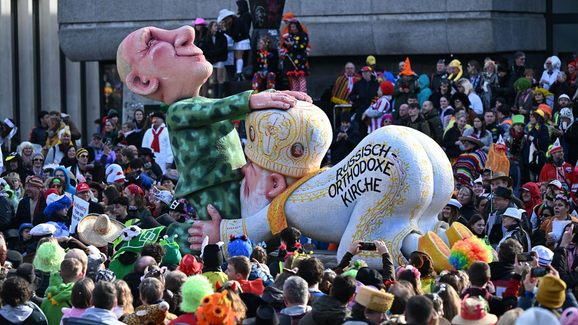 Der Mottowagen, der Russlands Präsidenten Putin zeigt, der im Military-Outfit auf dem Boden kniet und die Hände auf den Kopf des russischen Patriarchen legt.