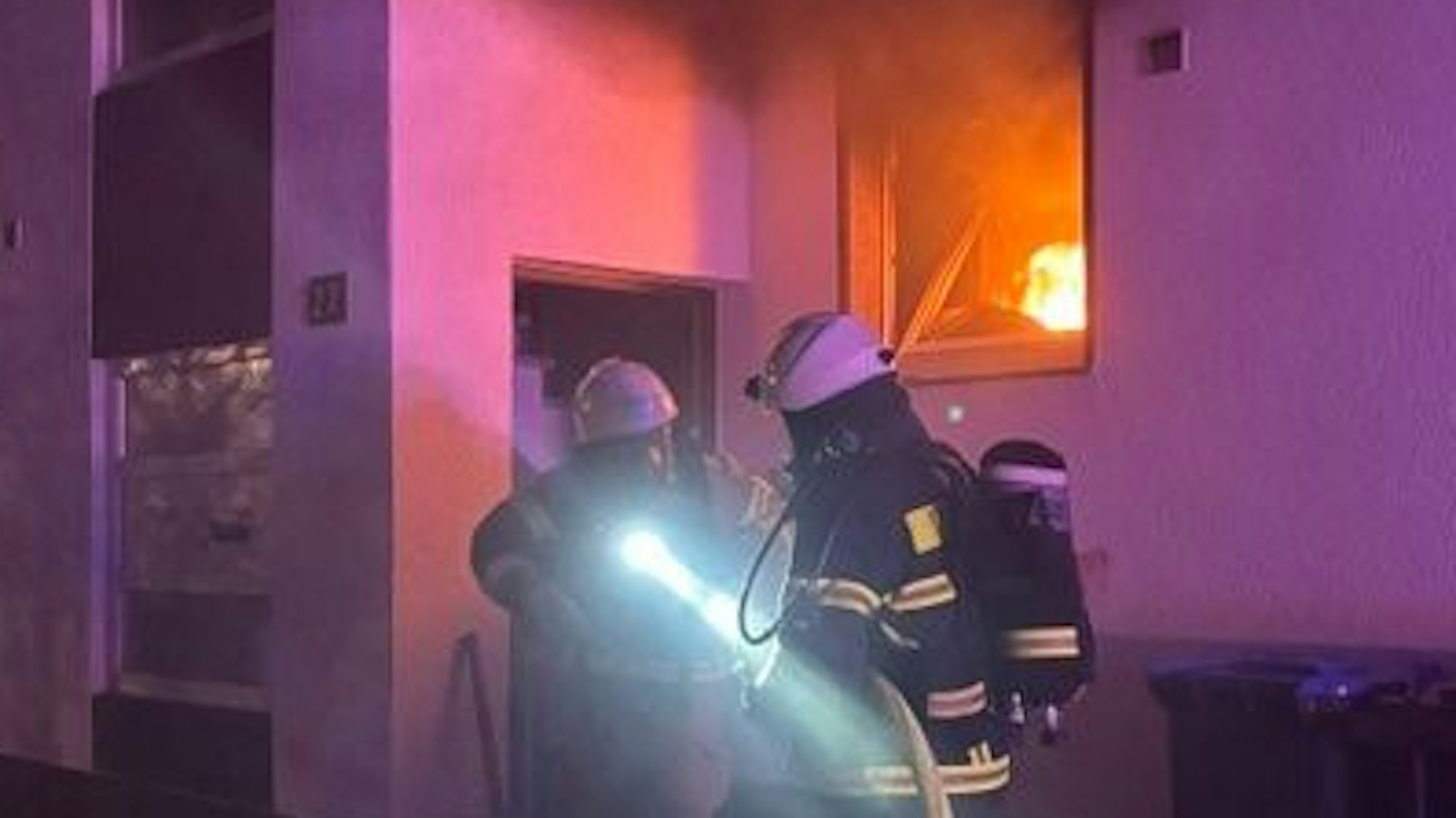 Das Bild zeigt Einsatzkräfte der Feuerwehr vor einer brennenden Wohnung.