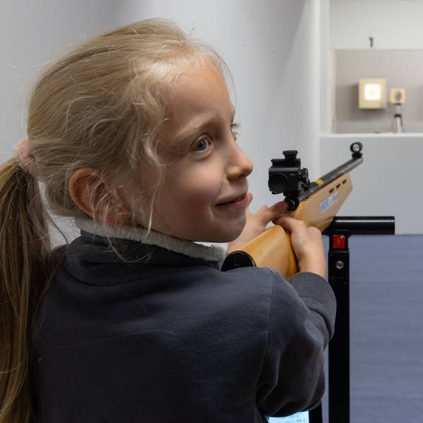 Ein Mädchen zielt mit einem Laser-Lichtpunkt-Gewehr auf eine Zielschiebe mit einem Osterei.