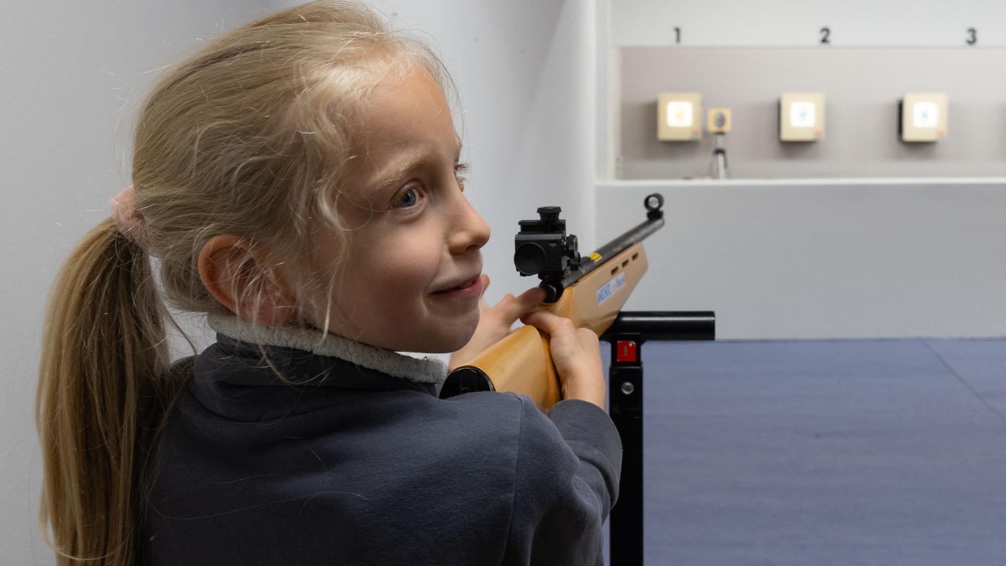 Ein Mädchen zielt mit einem Laser-Lichtpunkt-Gewehr auf eine Zielschiebe mit einem Osterei.