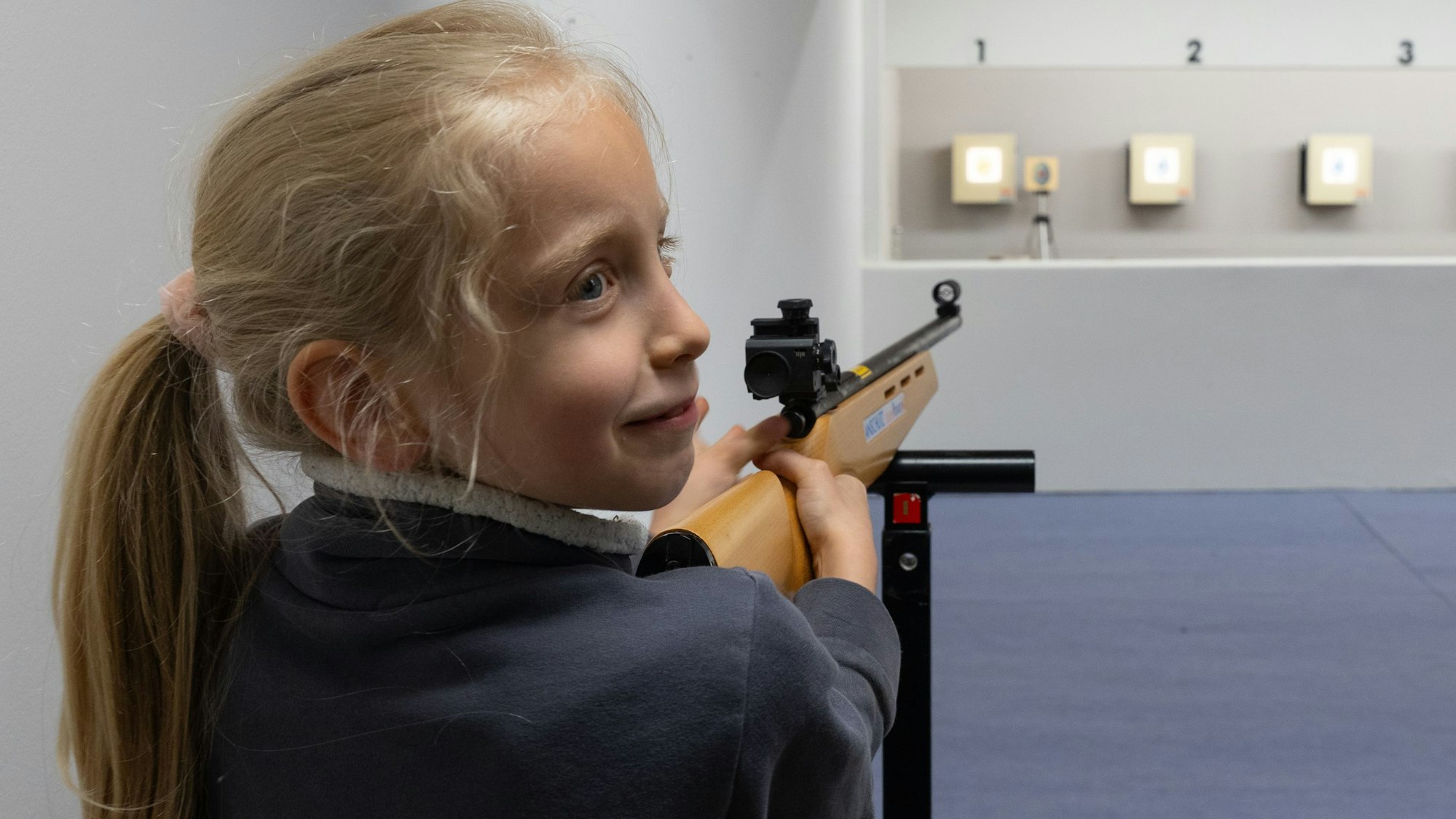 Ein Mädchen zielt mit einem Laser-Lichtpunkt-Gewehr auf eine Zielschiebe mit einem Osterei.