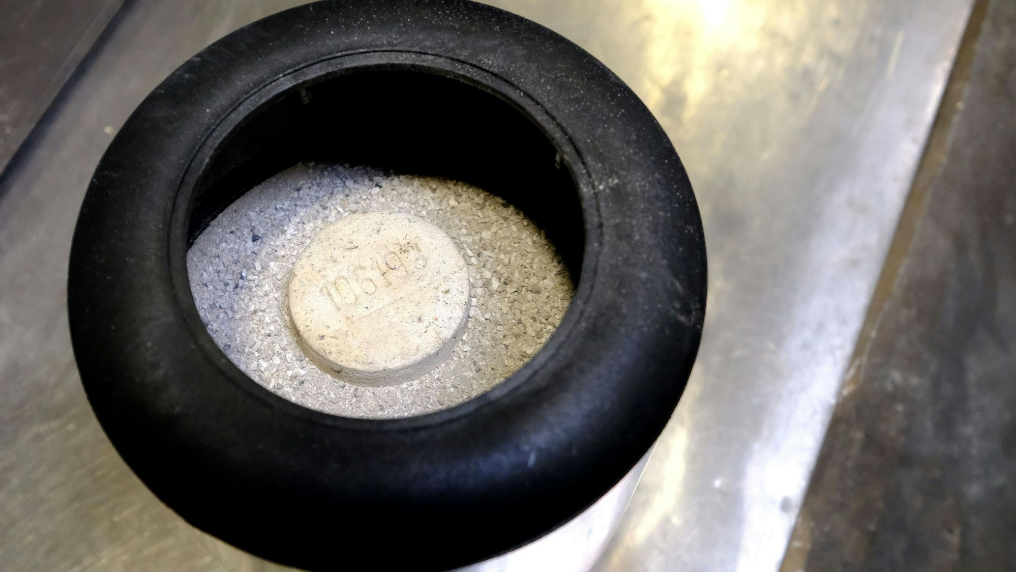 Asche in einer Transport-Urne. Obenauf liegt ein Stein mit einer eingeprägten Nummer, um ein Vertauschen der Asche zu verhindern.