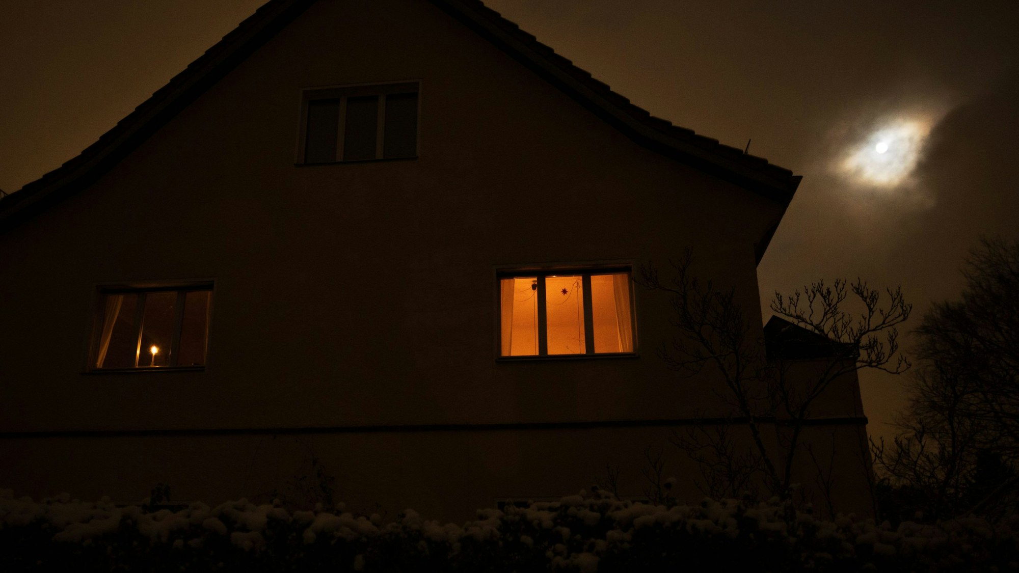 Das Bild zeigt ein Haus in der Nacht, das durch Kerzenschein beleuchtet ist.