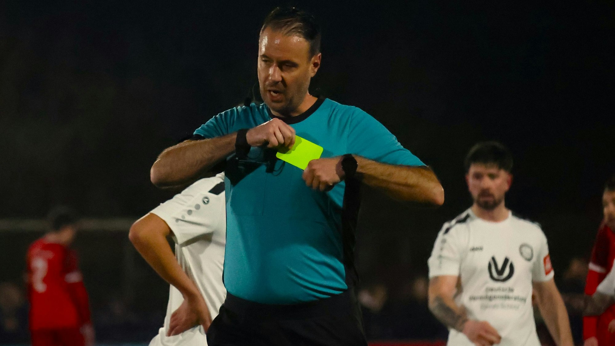 Schiedsrichter Niklas Granrath steckt sich die Gelbe Karte in die Brusttasche.