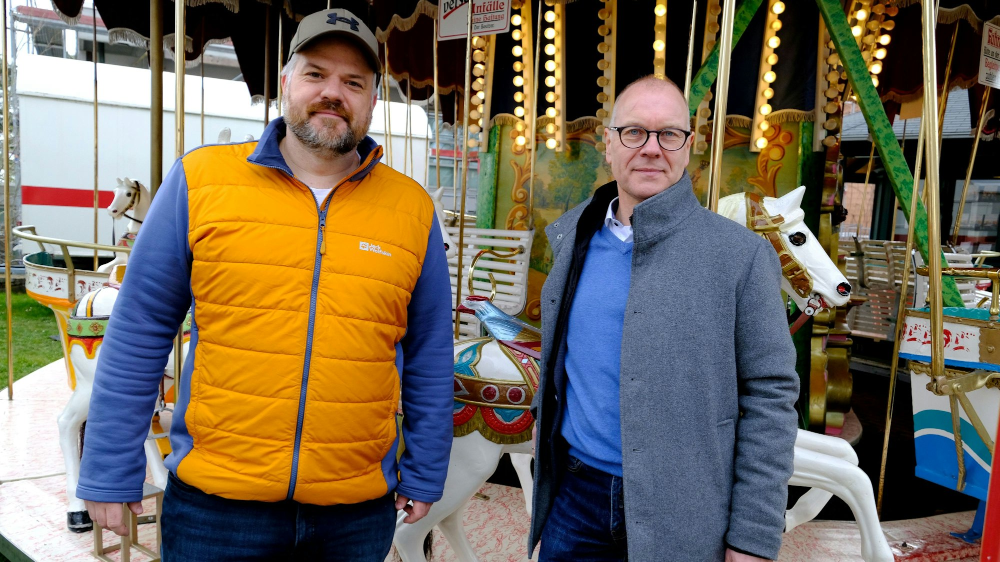 Die beiden Männer stehen vor einem historischen Kinderkarussell auf dem Jahrmarkt anno dazumal im Freilichtmuseum Kommern.