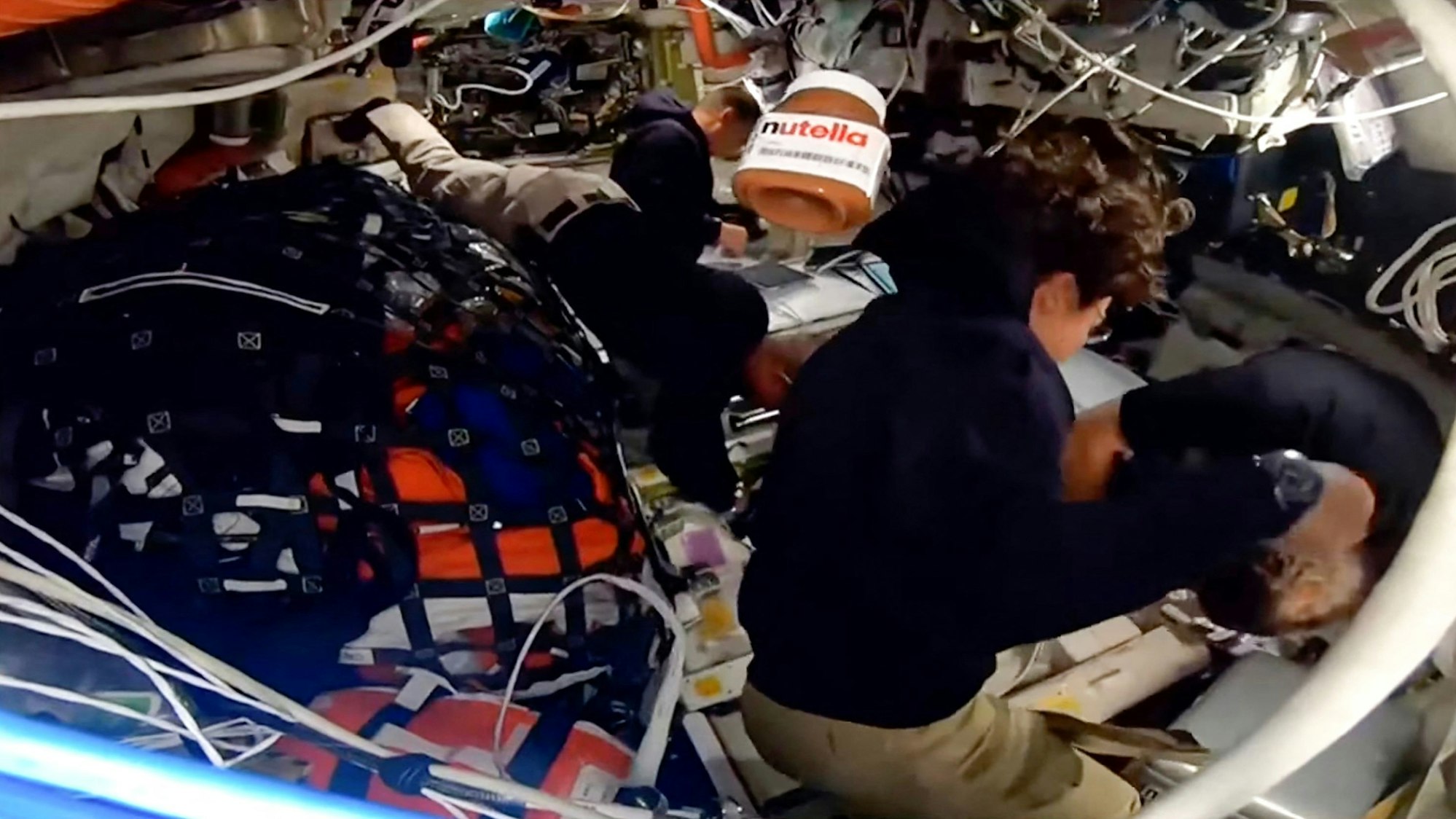 Dieser Screenshot aus einem NASA-Livestream zeigt ein Glas Nutella, das an Bord des Raumschiffs Orion schwebt, während die Besatzungsmitglieder Victor Glover, Reid Wiseman, Jeremy Hansen und Christina Koch arbeiten.