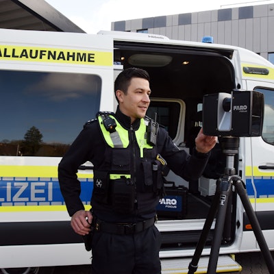 Zu sehen ist ein Polizist vor einem Polizeiwagen, der einen Scanner bedient.