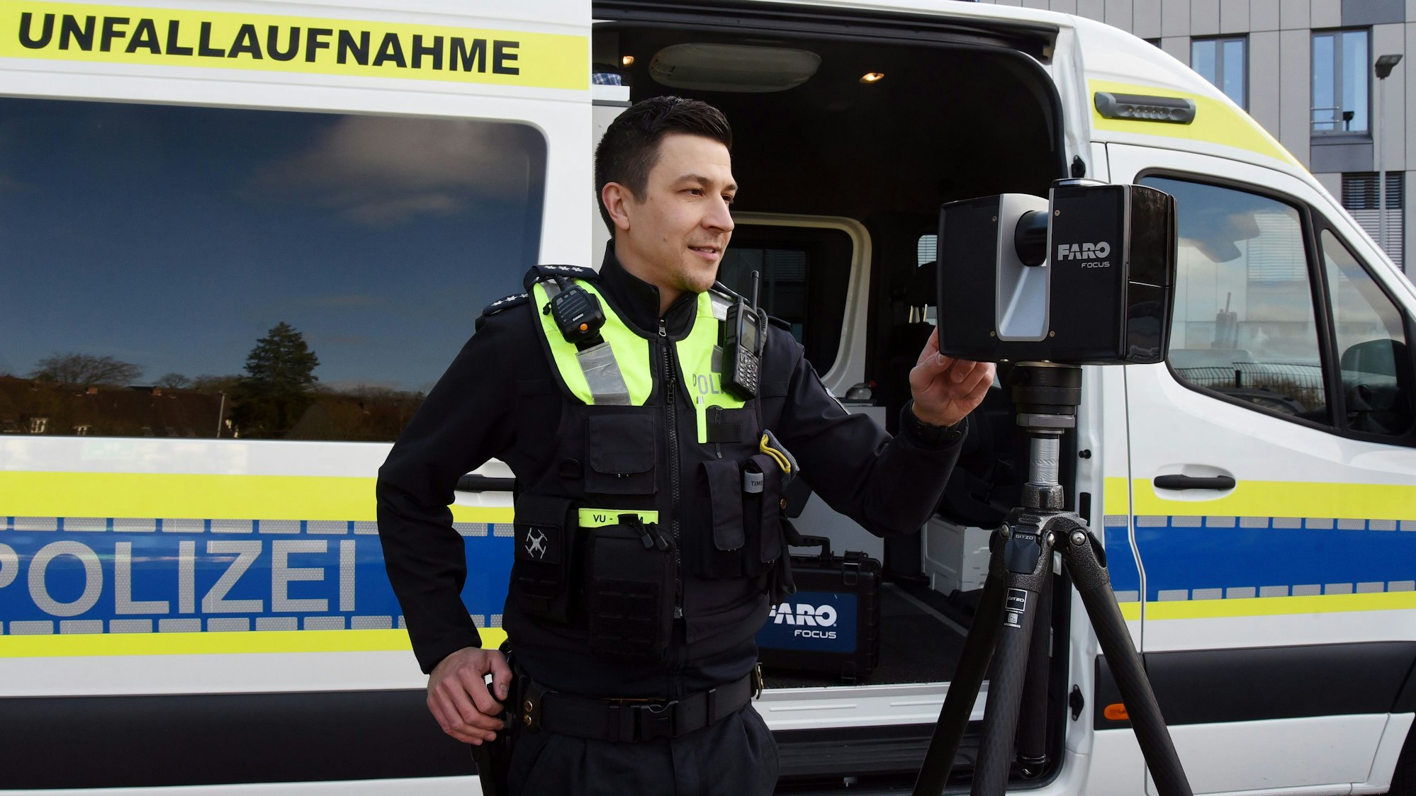 Zu sehen ist ein Polizist vor einem Polizeiwagen, der einen Scanner bedient.