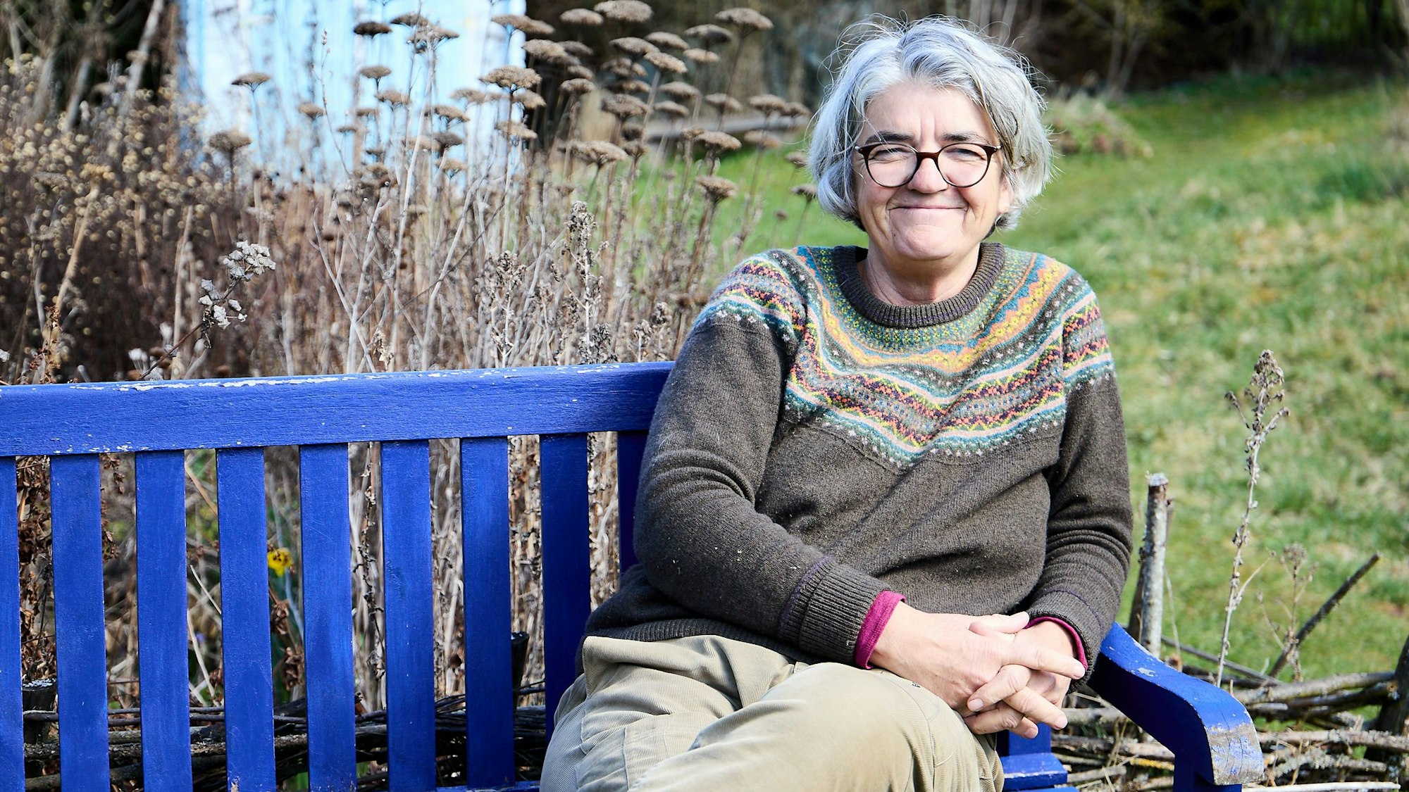 Ulrike Kreuer sitzt in ihrem Garten in Nettersheim auf einer blauen Bank.