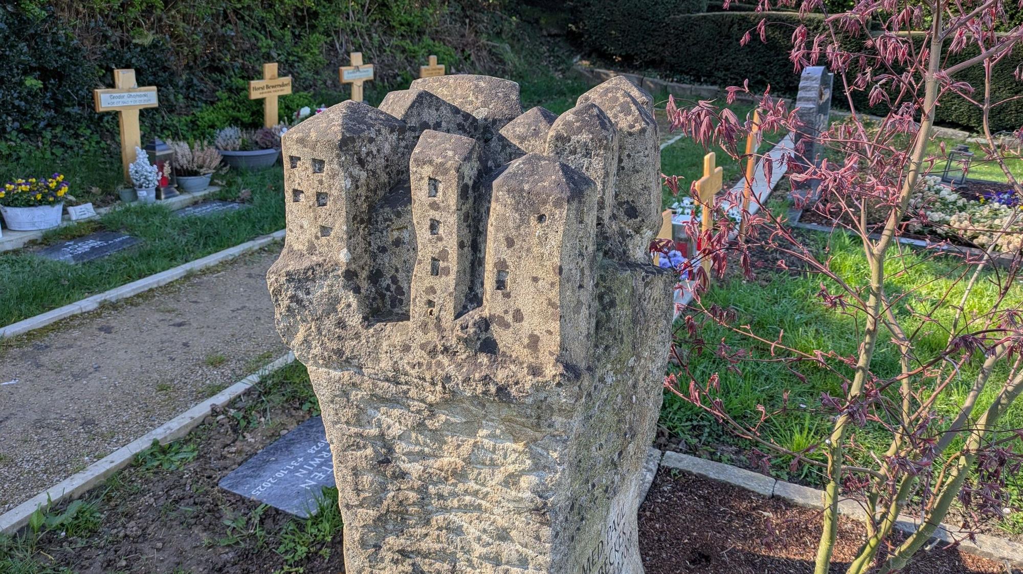 Ein Felsendorf ziert die Krone dieses Grabsteins auf dem Friedhof.