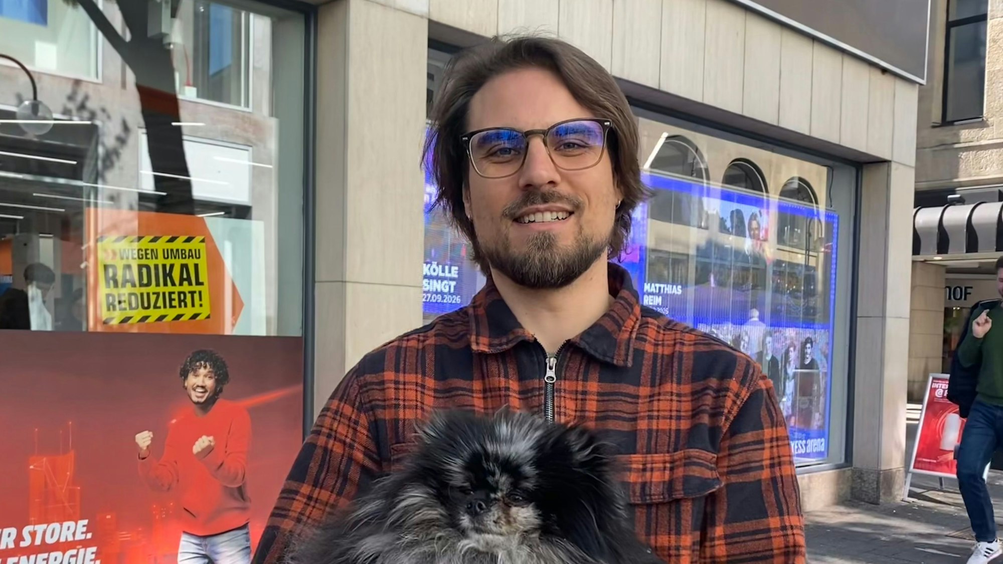 Ein Mann mit Hund im Arm schaut in die Kamera.