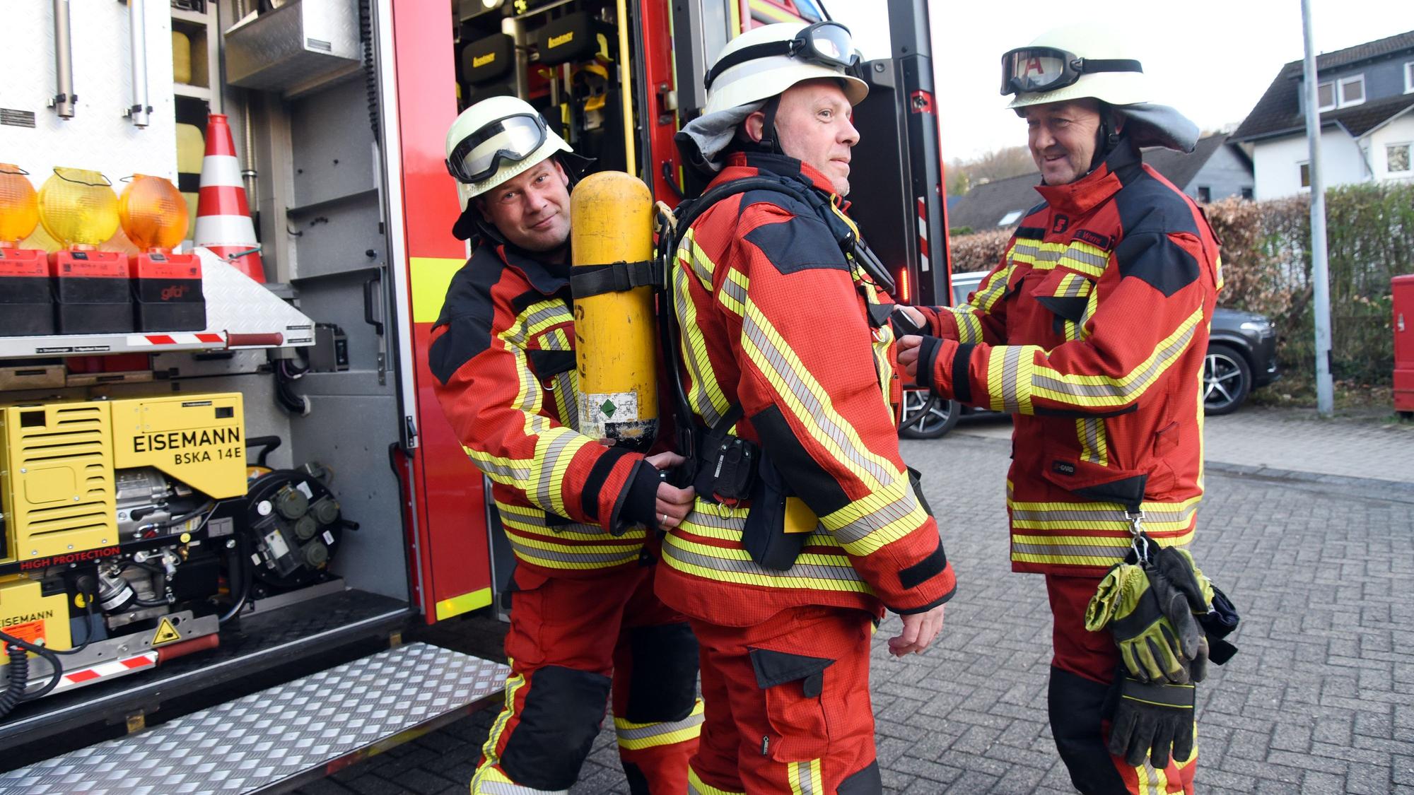 Drei Feuerwehrleute stehen an einem Feuerwehrauto.