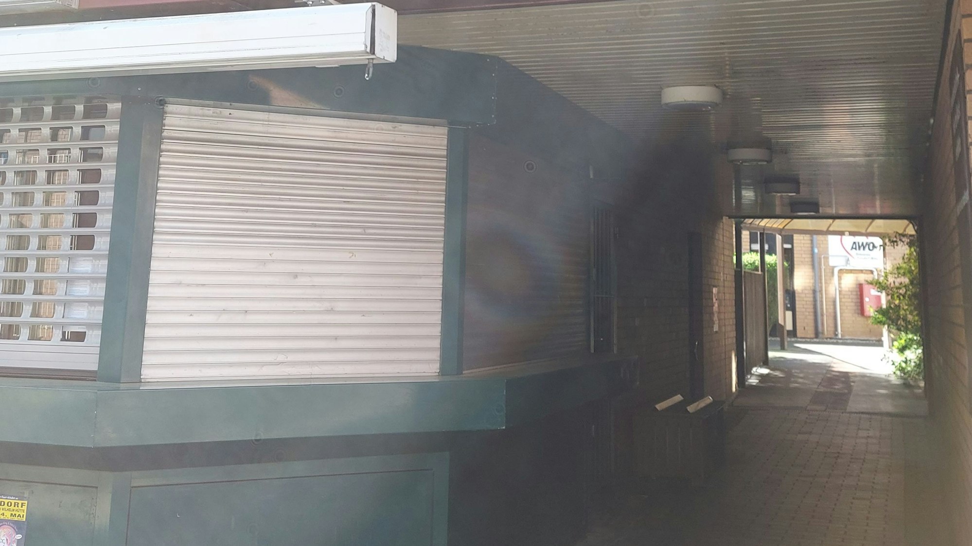 Ein schmaler Durchgang durch eine Bebauung, links ein geschlossener Kiosk.