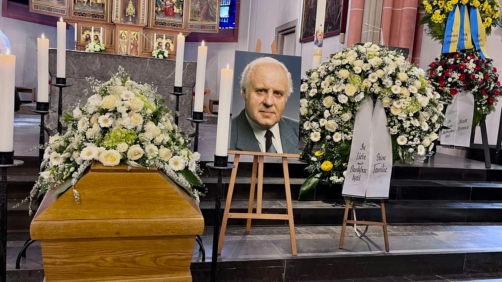 Vor dem Altar sind der Sarg, ein Foto des Verstorbenen und Blumenschmuck zu sehen.