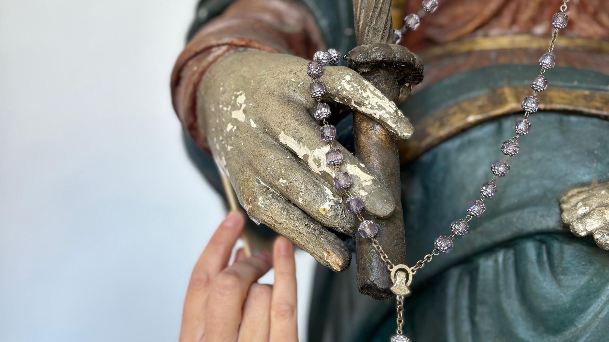 Nahaufnahme auf eine Hand die einen Wattestab an die Hand einer Marien-Figur anlegt.