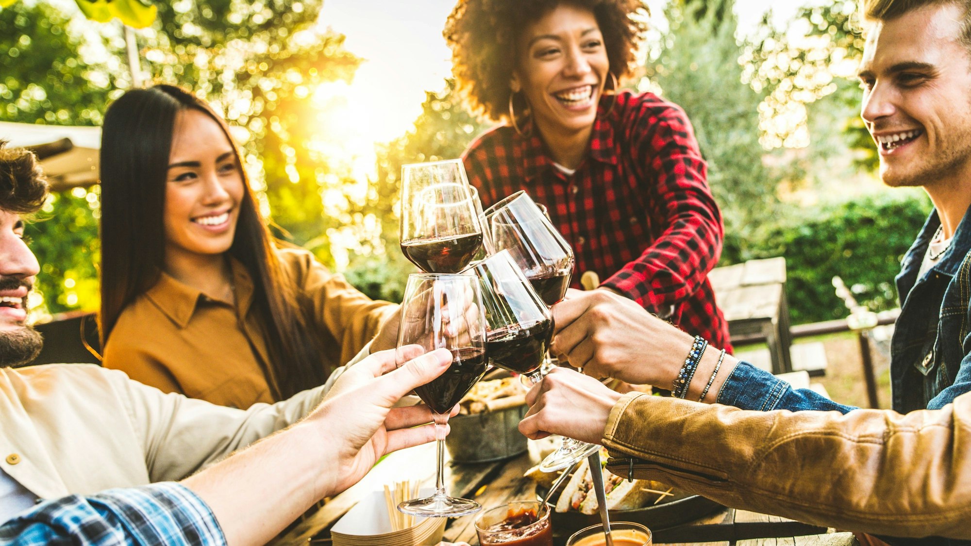 Eine Gruppe von Freunden, die sich beim Abendessen an Holztischen amüsieren.