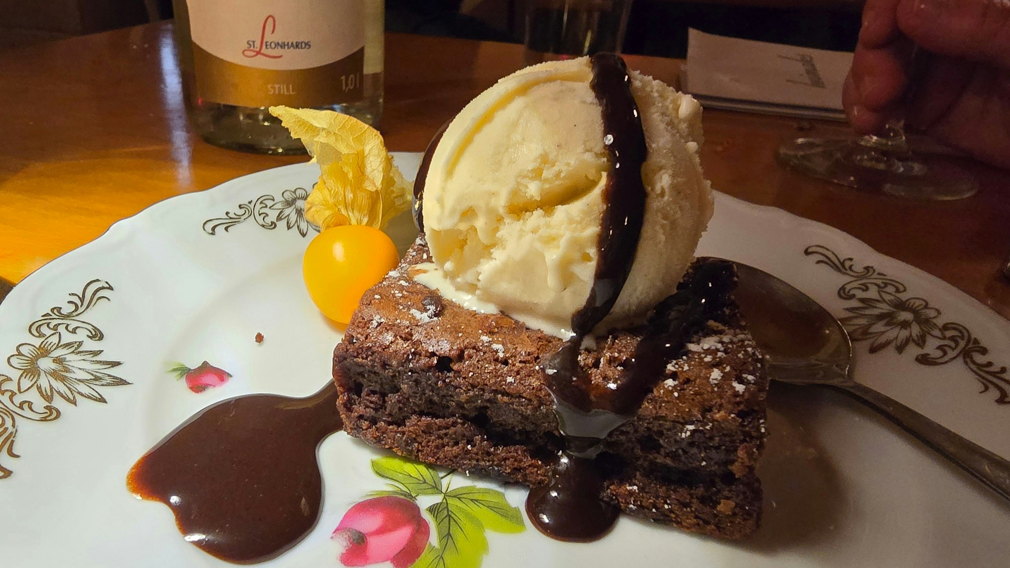 Auf einem Teller mit Verschnörkelungen ist ein Schokobrownie mit Vanilleeis und Schokosauce angerichtet.