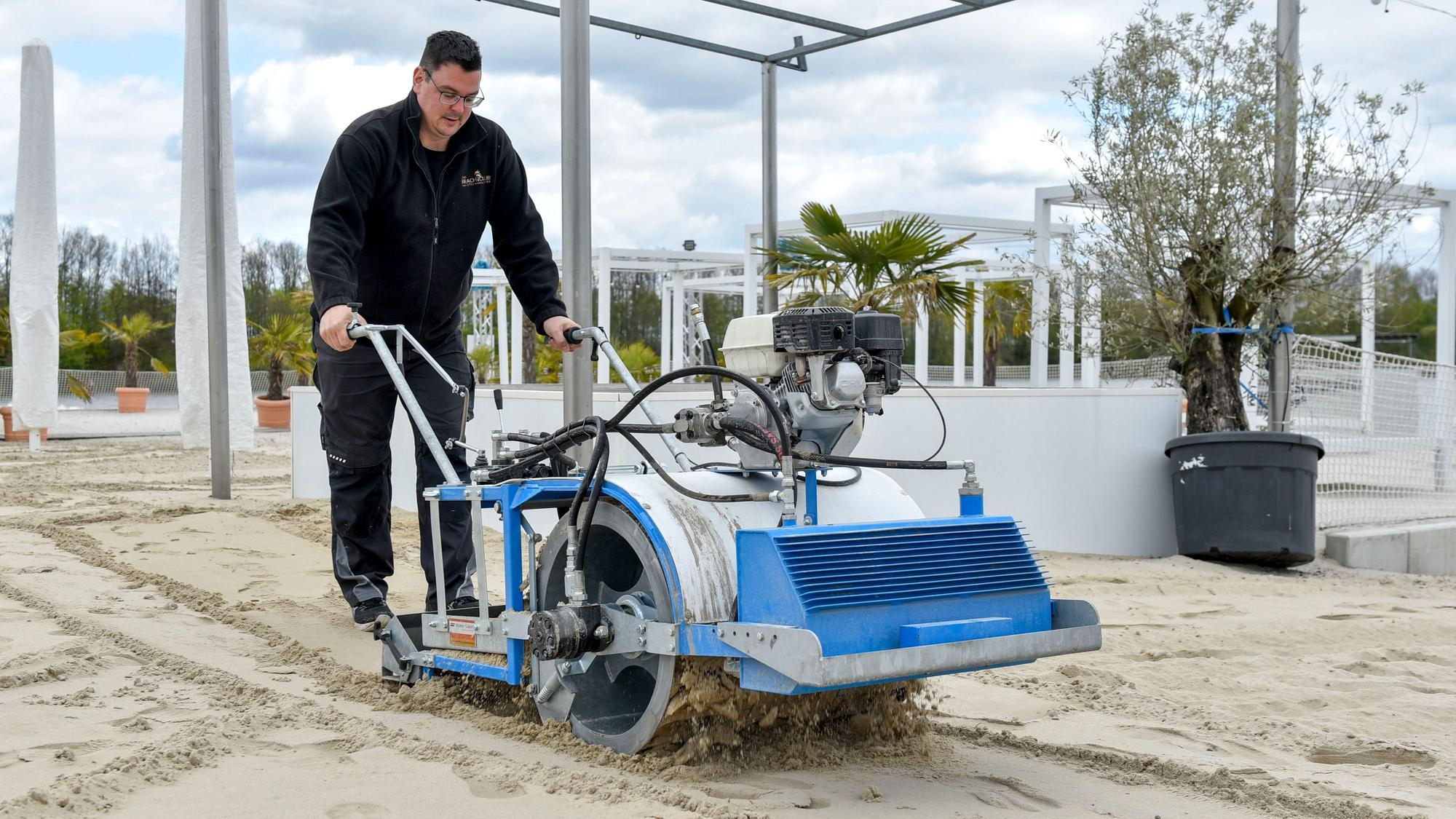 Zu sehen ist ein Mann, der eine Sandreinigungsmaschine schiebt.