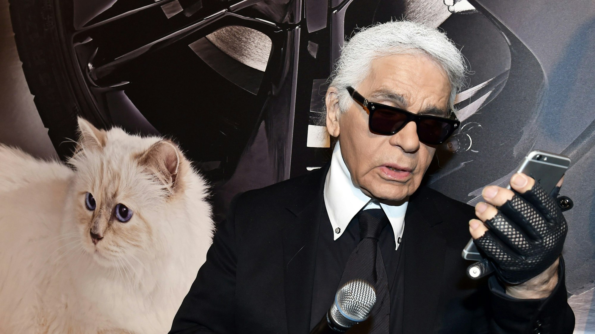 Der Modedesigner Karl Lagerfeld blickt neben einem Foto seiner Birma-Katze Choupette auf sein Smartphone bei der Vernissage ‚Corsa Karl und Choupette‘ im Palazzo Italia.