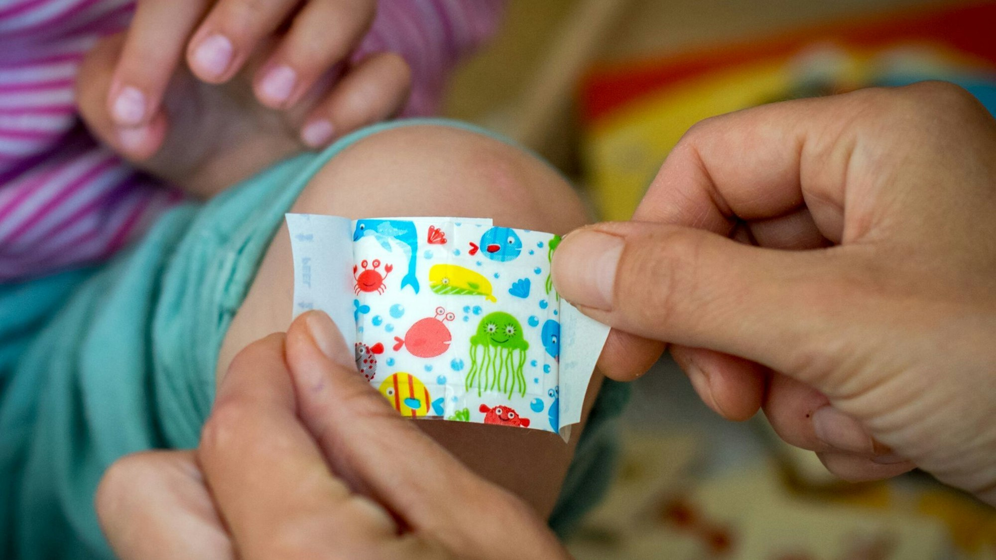 Eine Mutter klebt ihrer Tochter ein buntes Pflaster aufs Knie