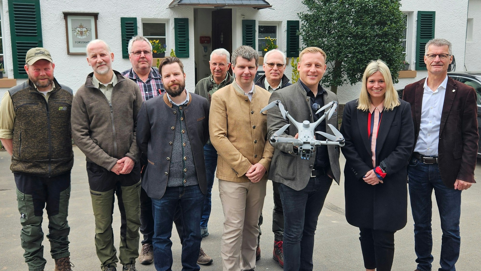 Neun Männer und eine Frau stehen nebeneinander, einer präsentiert eine Drohne.