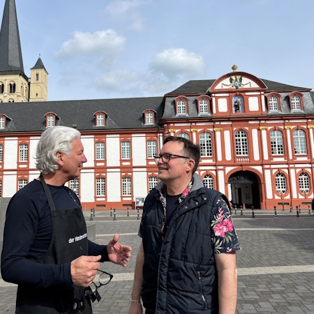 Zwei Männer im Gespräch, im Hintergrund die Abtei Brauweiler.