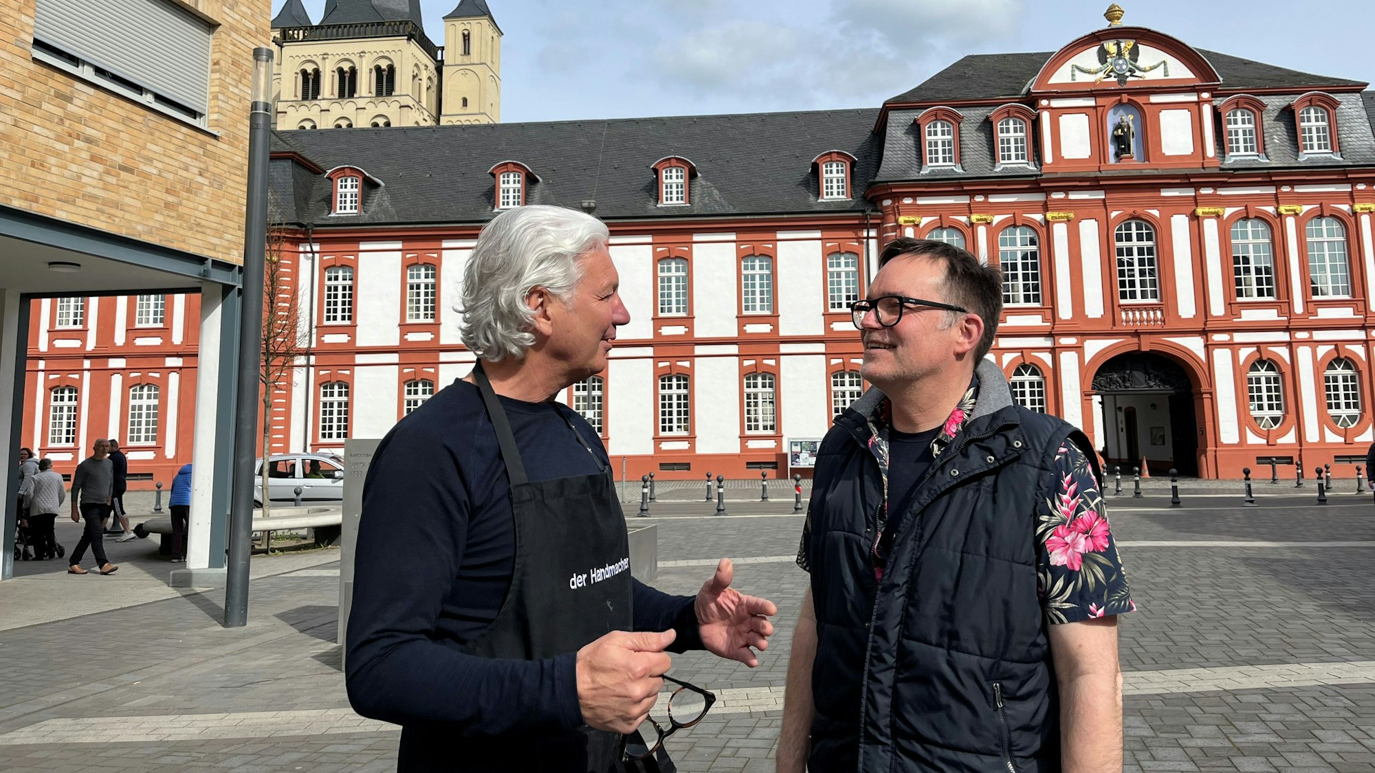 Zwei Männer im Gespräch, im Hintergrund die Abtei Brauweiler.