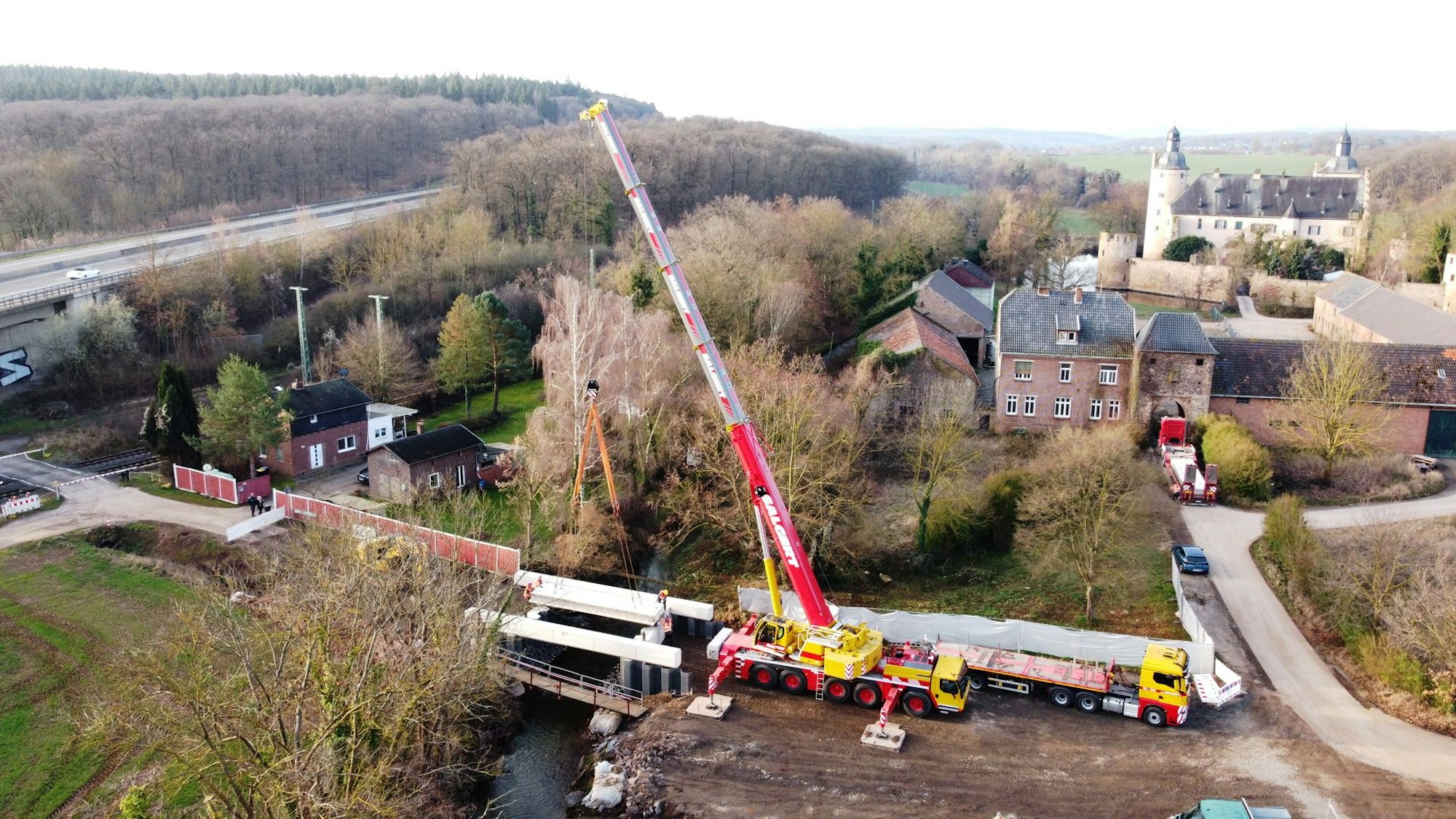 Die Drohnenaufnahme zeigt die Montage der neuen Veybachbrücke mit einem Schwerlastkran. Im Hintergrund ist die Burg Veynau zu erkennen.