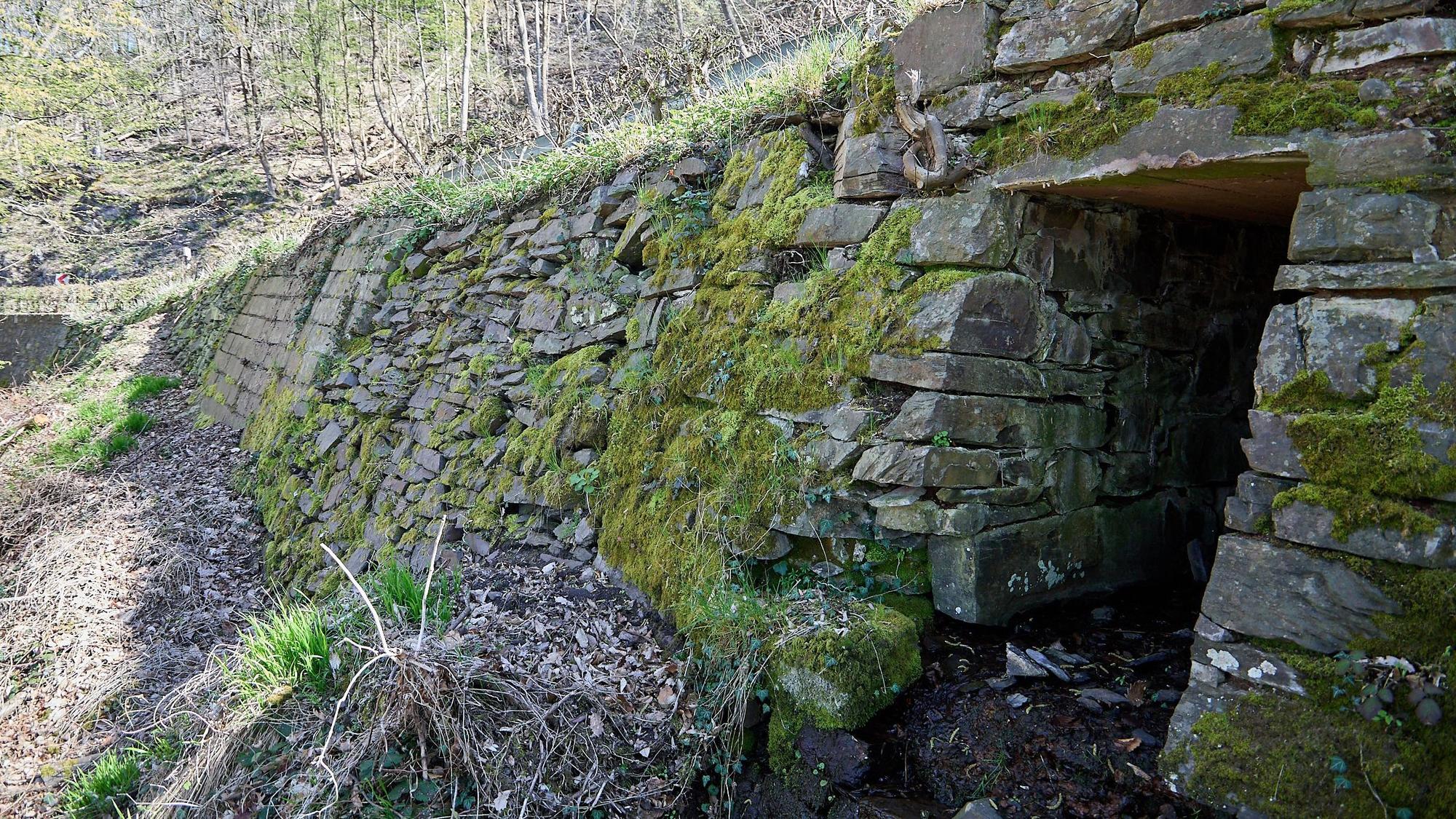 Das Bild zeigt eine von Moos bewachsene Trockenmauer. Nicht zu sehen ist die Straße, die sie trägt.