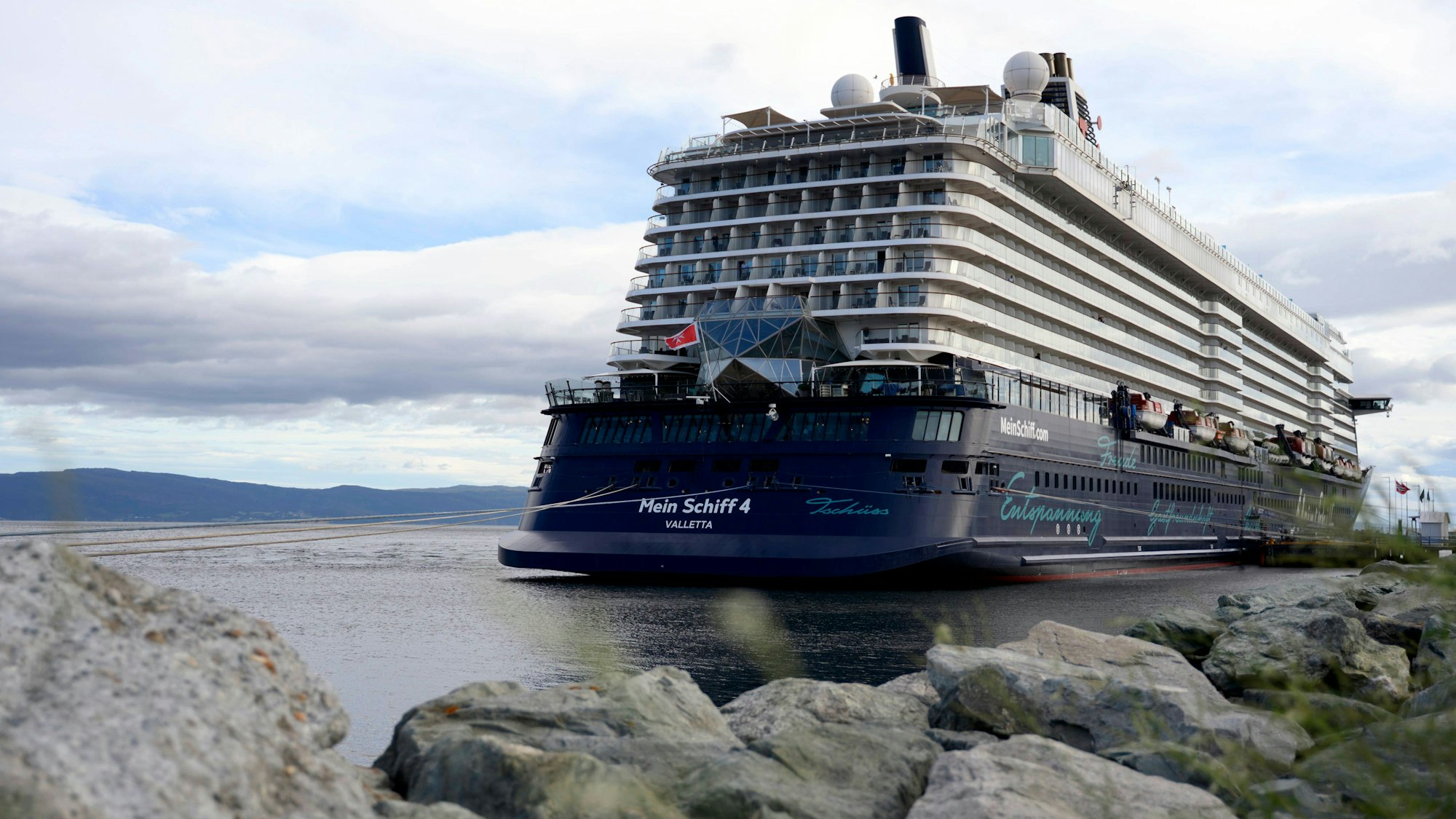 Kreuzfahrtschiff am Wasser mit Bergen und Felsen.